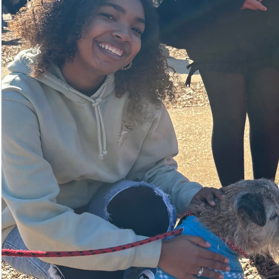 Woman smiling and petting a dog outdoors on a sunny day.