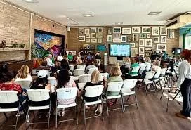People attending a seminar or workshop in a cozy room with a wall full of framed pictures and a large TV screen.