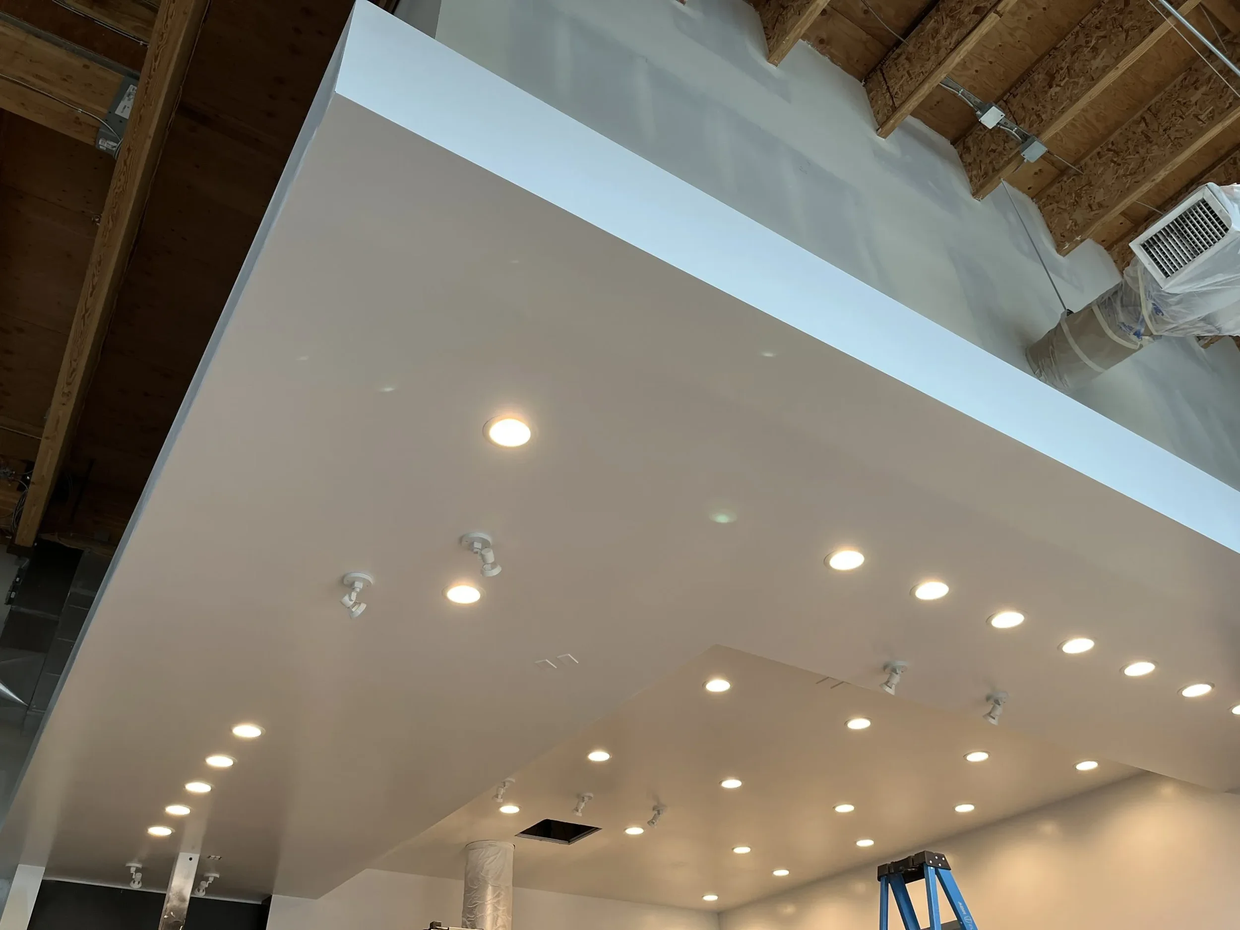 Ceiling with multiple recessed lights and track lighting, wooden beams, and an air vent.