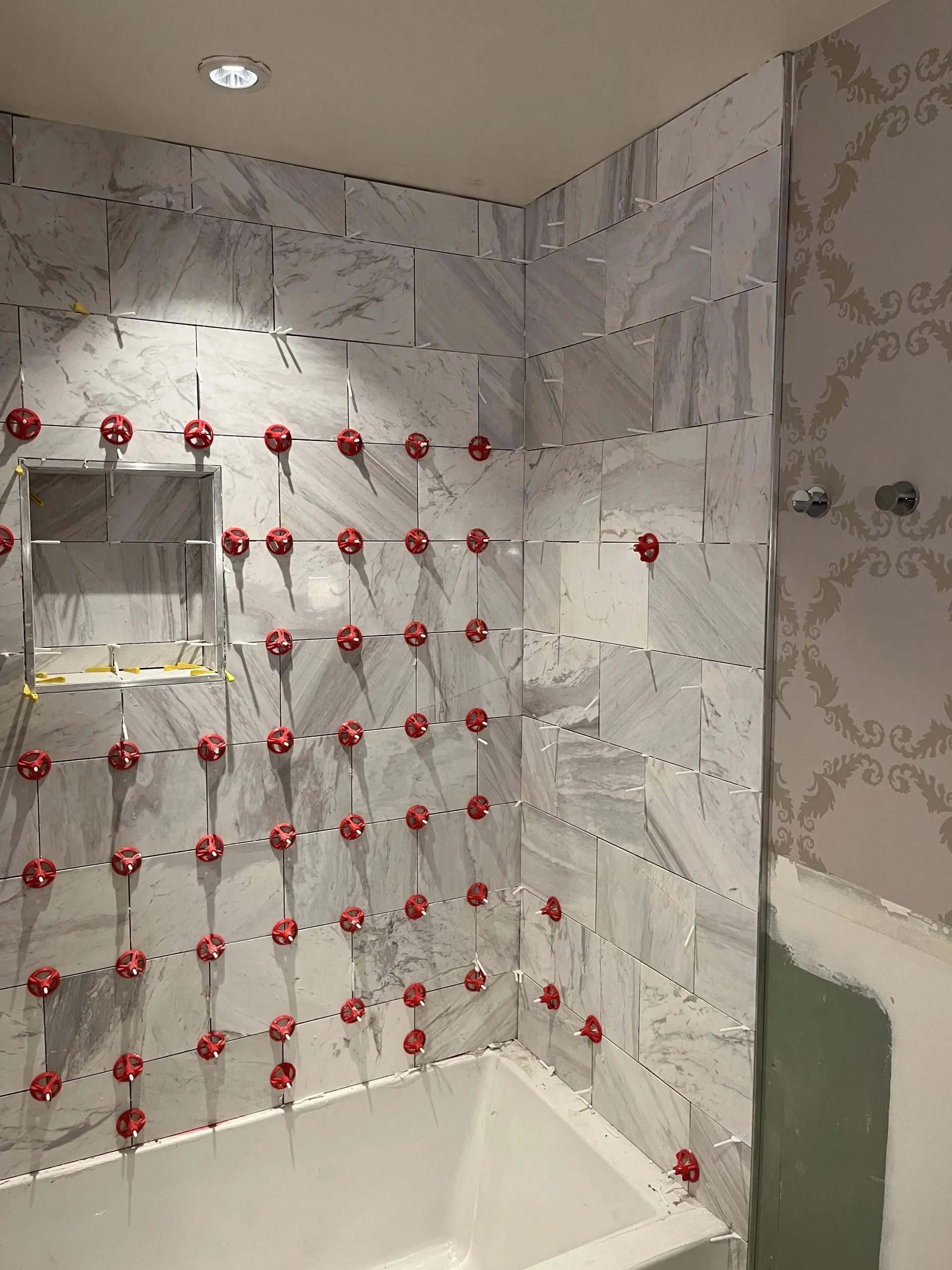 Bathroom shower area with marble tiles, red tile spacers, and a partial mirror on the wall.