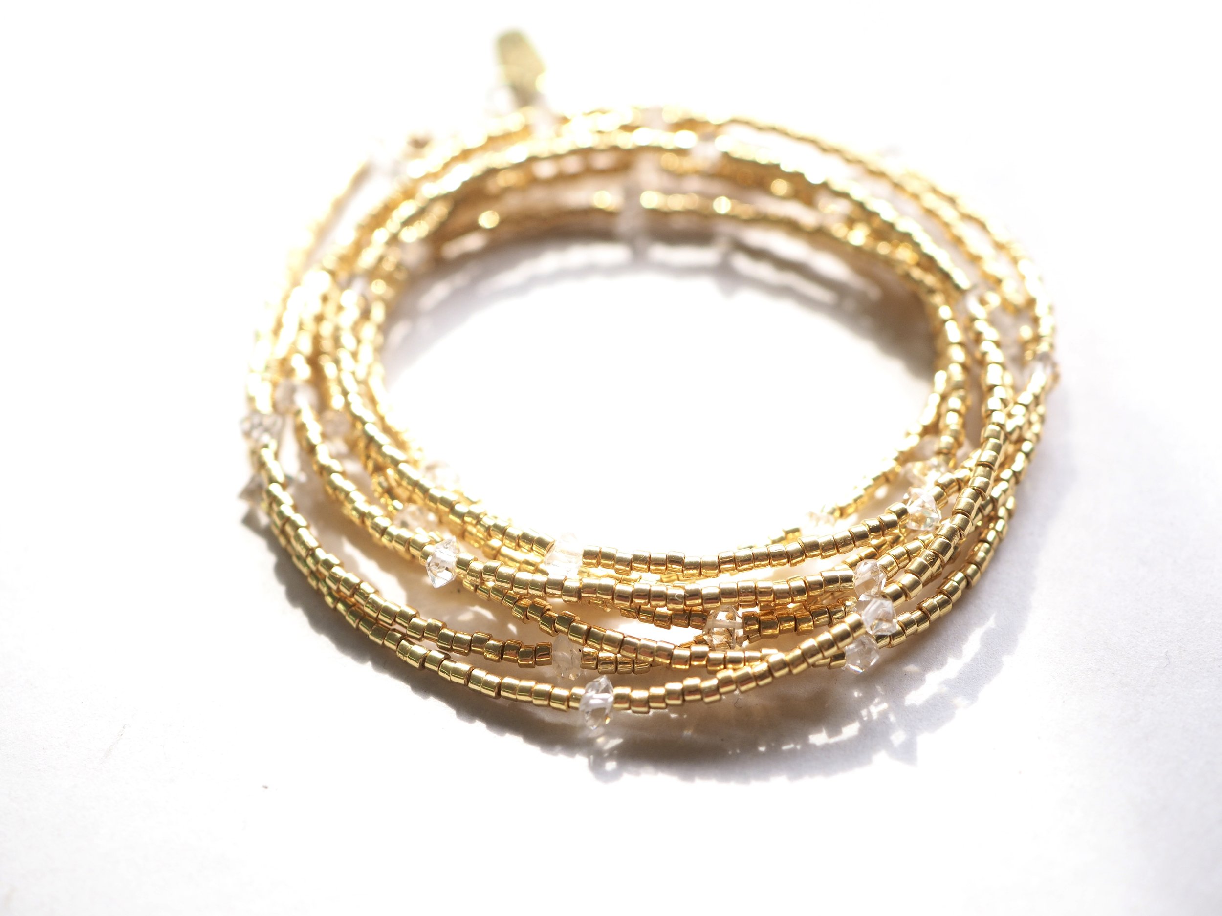 A gold multi-layered beaded bracelet with small clear beads, resting on a white surface.