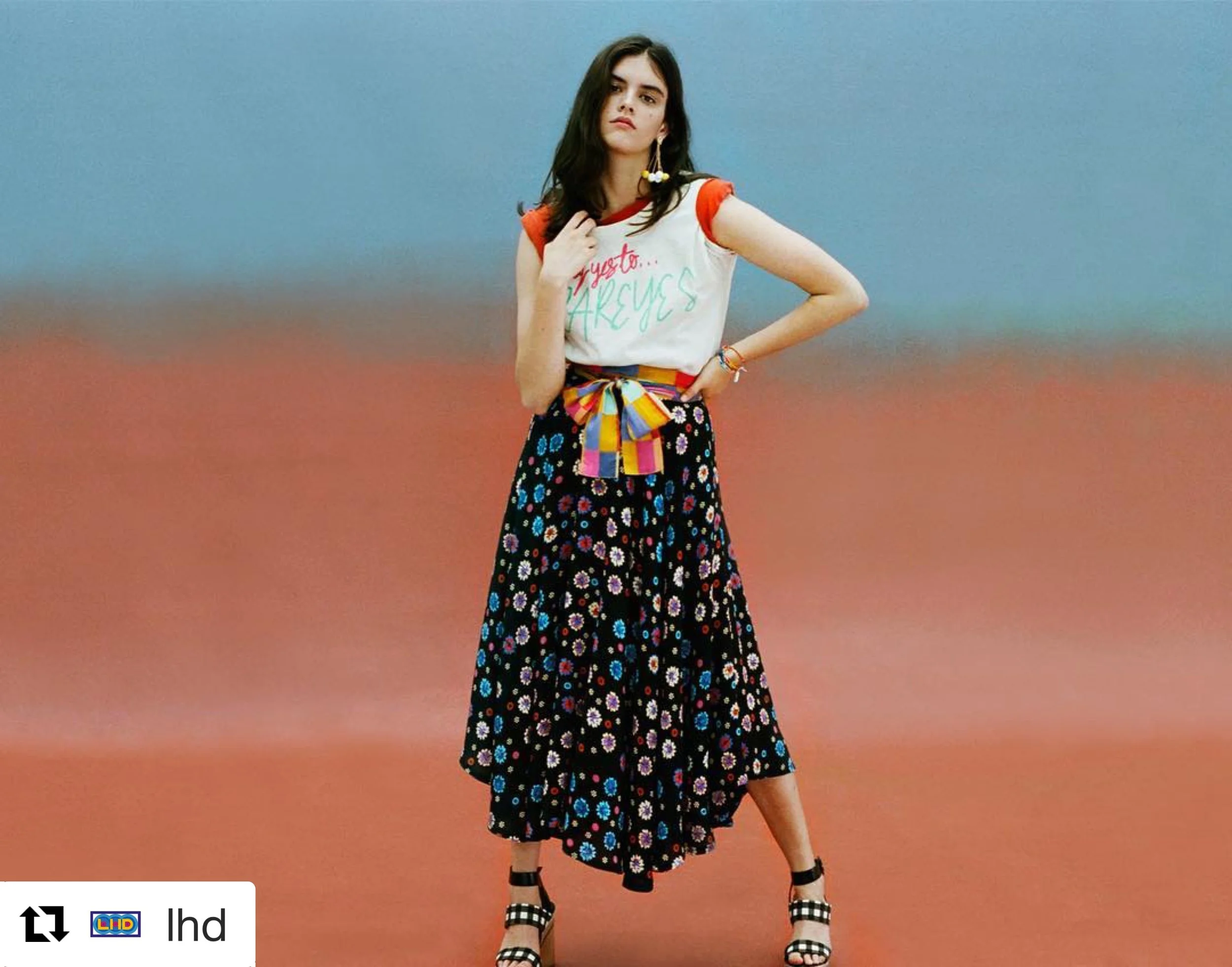 Young woman standing on colorful abstract background in a casual outfit, wearing a LHD white t-shirt with colorful writing, and Bunny Shapiro bracelets.