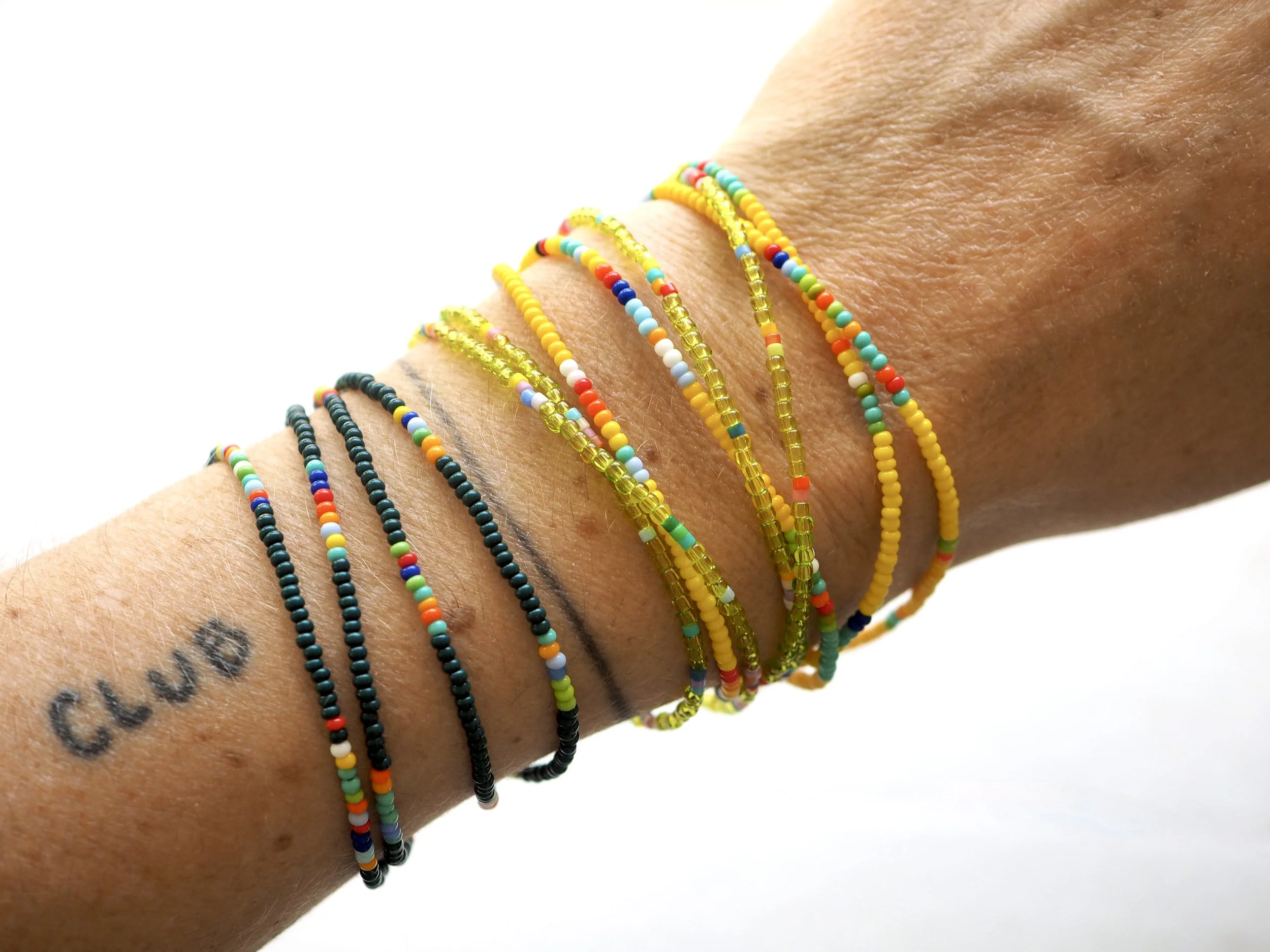 A person's arm with multiple colorful beaded bracelets and a tattoo that reads 'CLUB'.