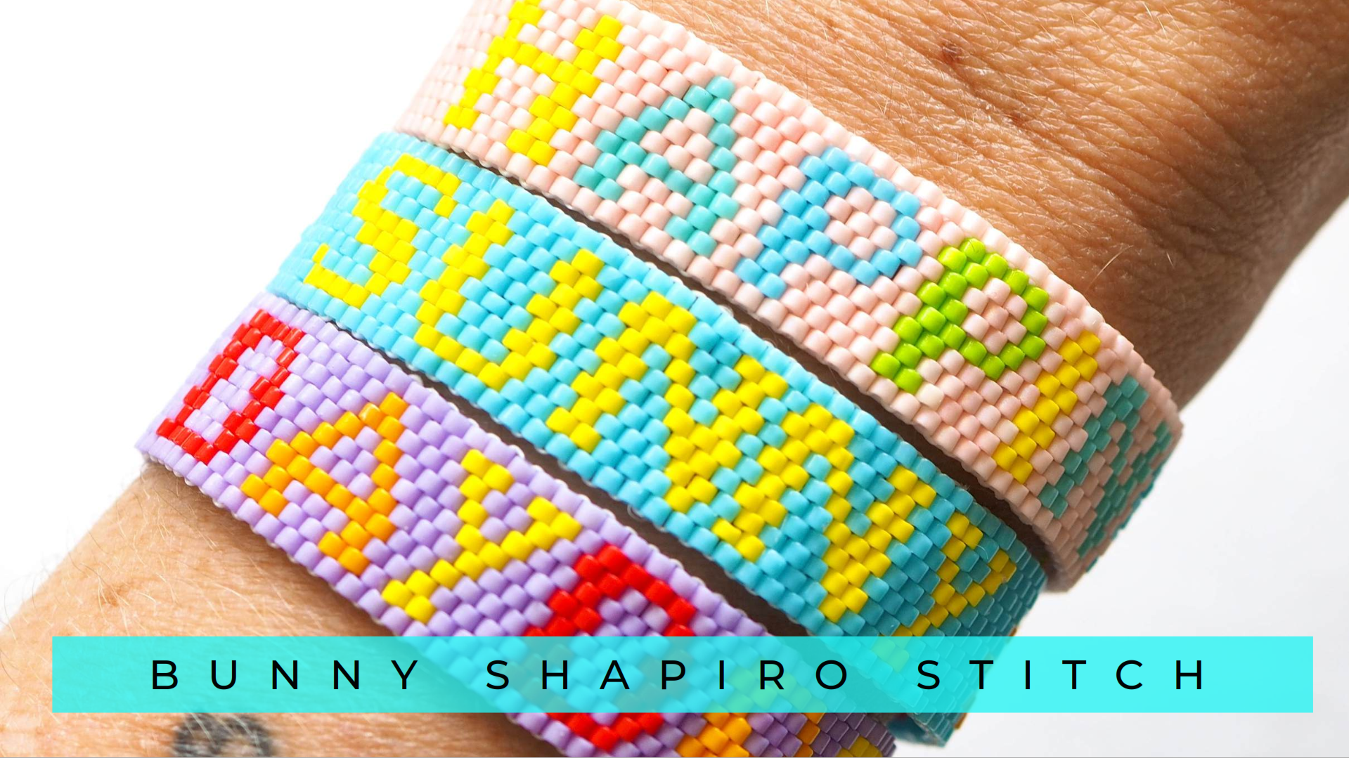 Close-up of a person's wrist with three colorful beaded bracelets, each with different words spelled out in yellow beads, including 'LOVE' and 'PEACE.' The bracelets are made with small, colorful beads and are stacked on the wrist. The background is plain white. Text overlay at the bottom reads 'BUNNY SHAPIRO STITCH' in black letters on a light blue background.