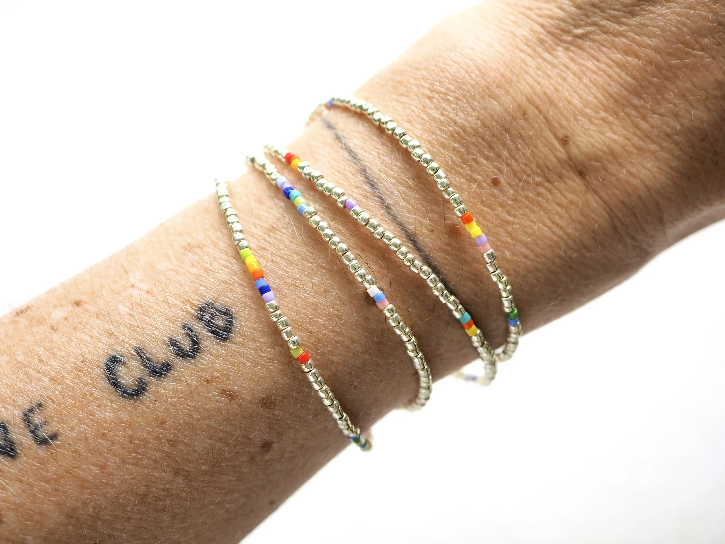 Three delicate beaded bracelets on a wrist with a tattoo.