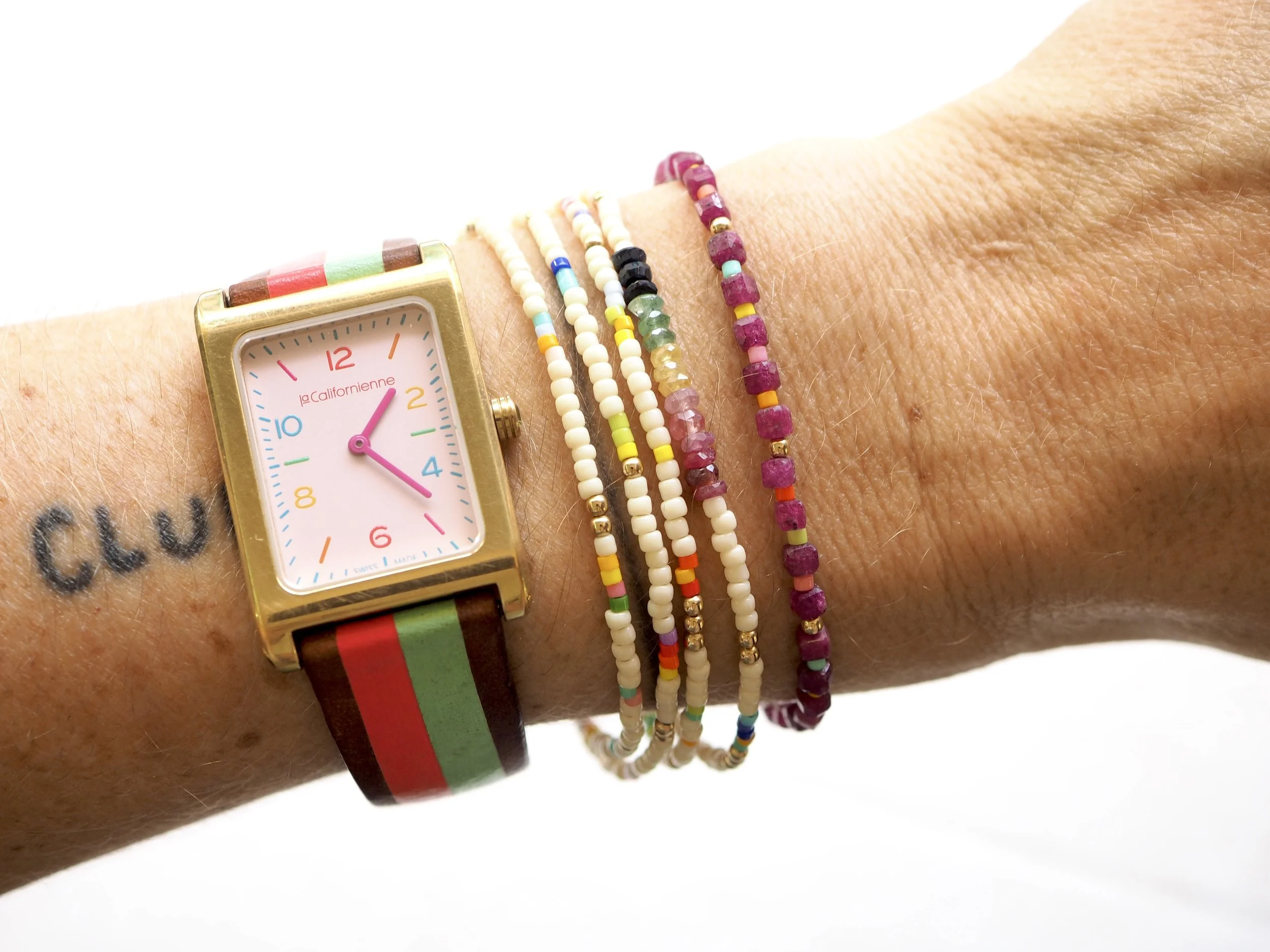 Close-up of a person's wrist wearing a colorful striped watch and multiple beaded bracelets.