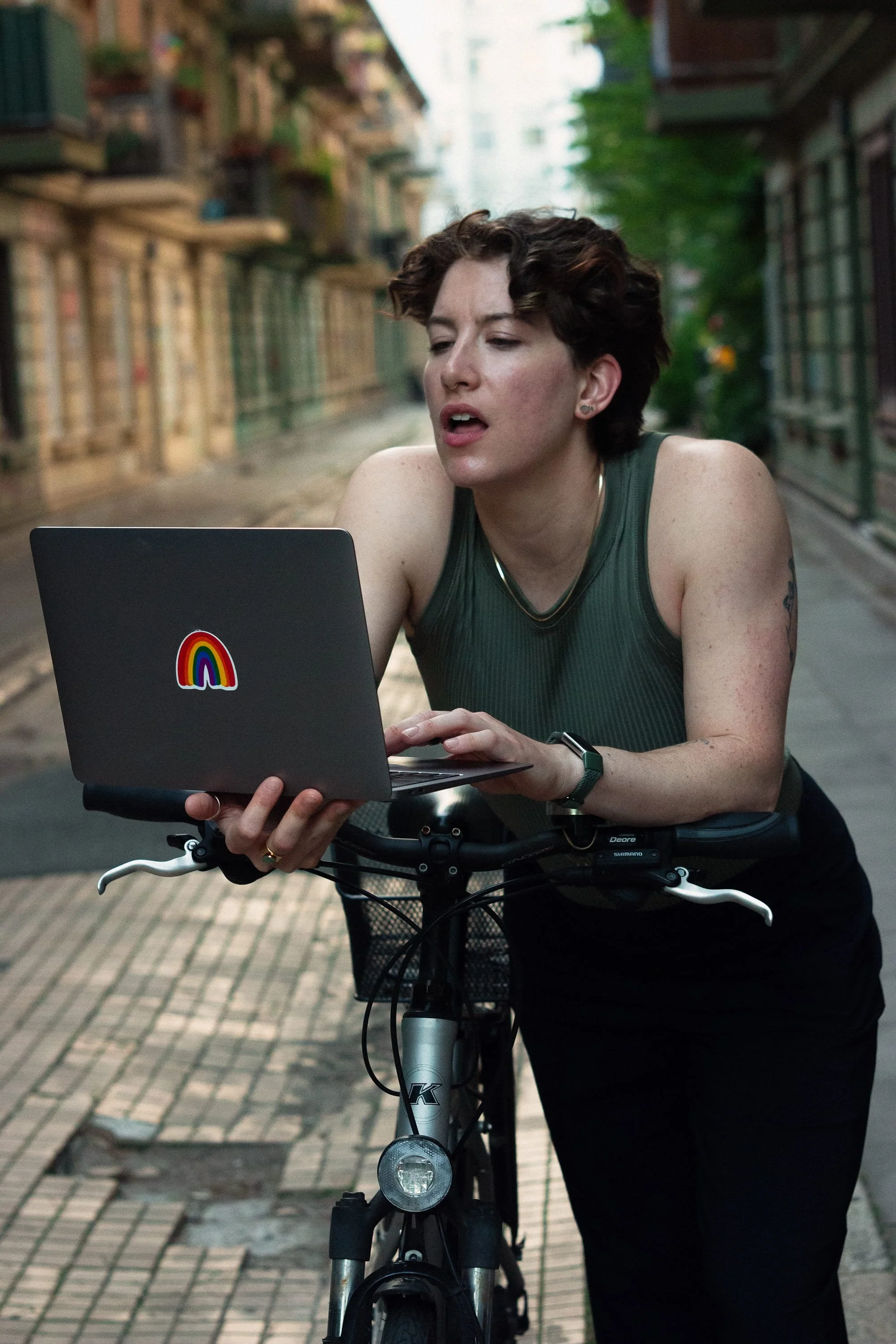 Maeve is leaning over a bicycle, holding a laptop, hard at work with a look of focus and concentration.