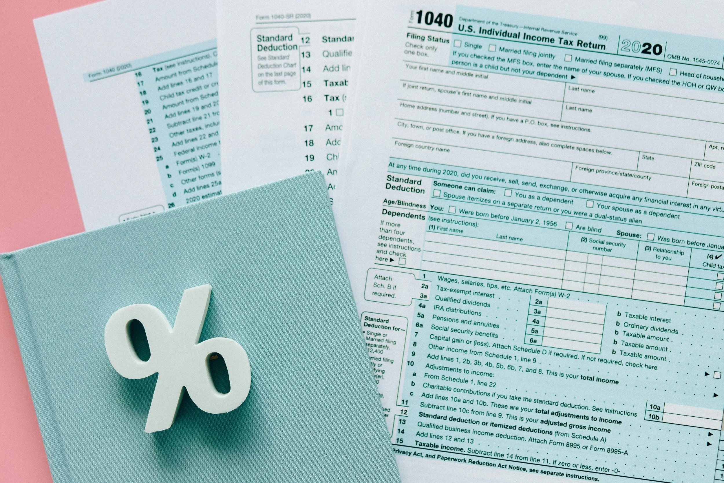U.S. 2020 individual income tax return forms, including a tax booklet, a secondary sheet, and a pink folder with a light blue cover featuring a white dollar sign symbol.