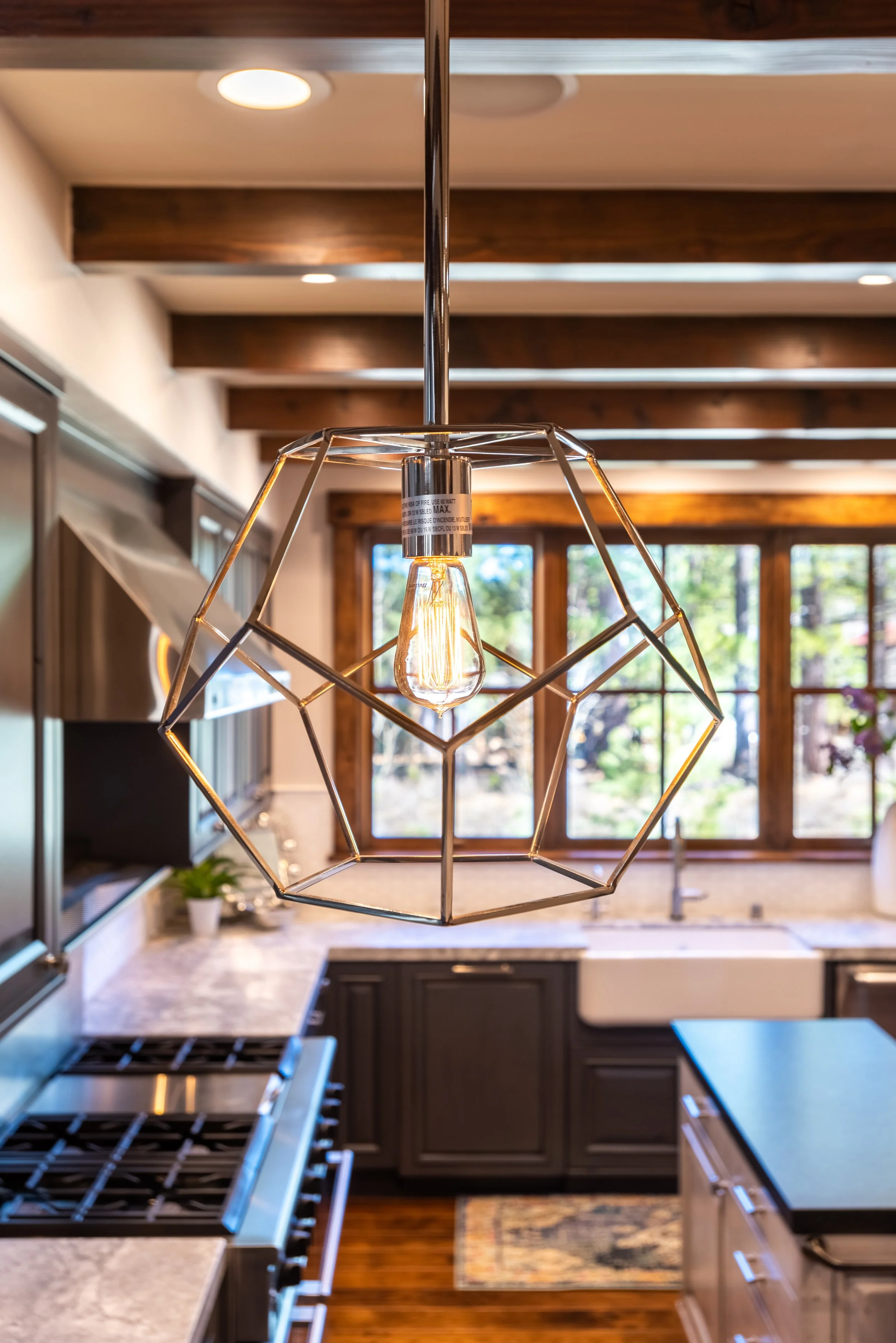 Modern pendant light with geometric metal frame hanging over a kitchen island in a bright kitchen
