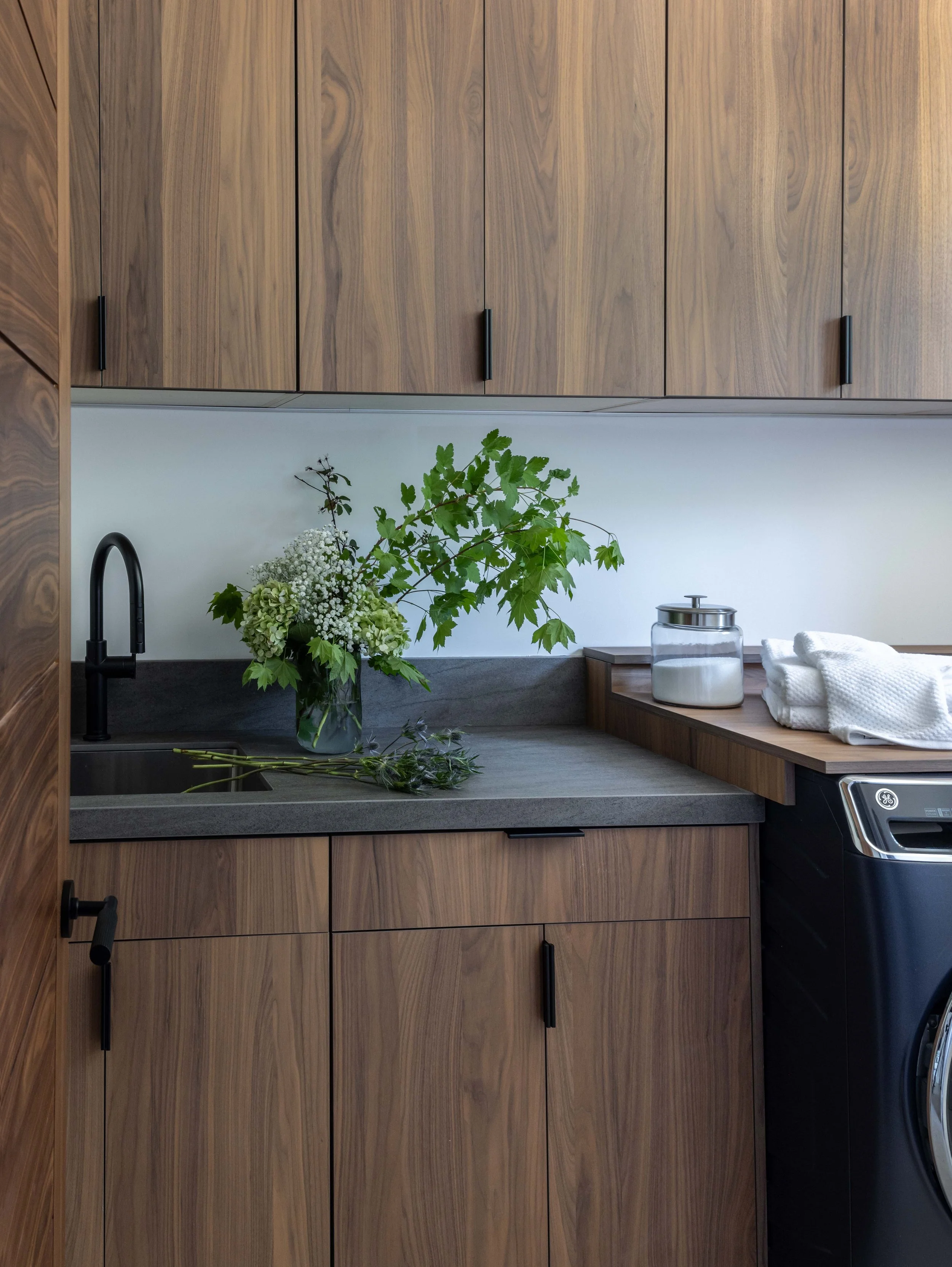 Modern kitchen with wooden cabinets, black faucet, gray countertop, and a bouquet of green and white flowers.