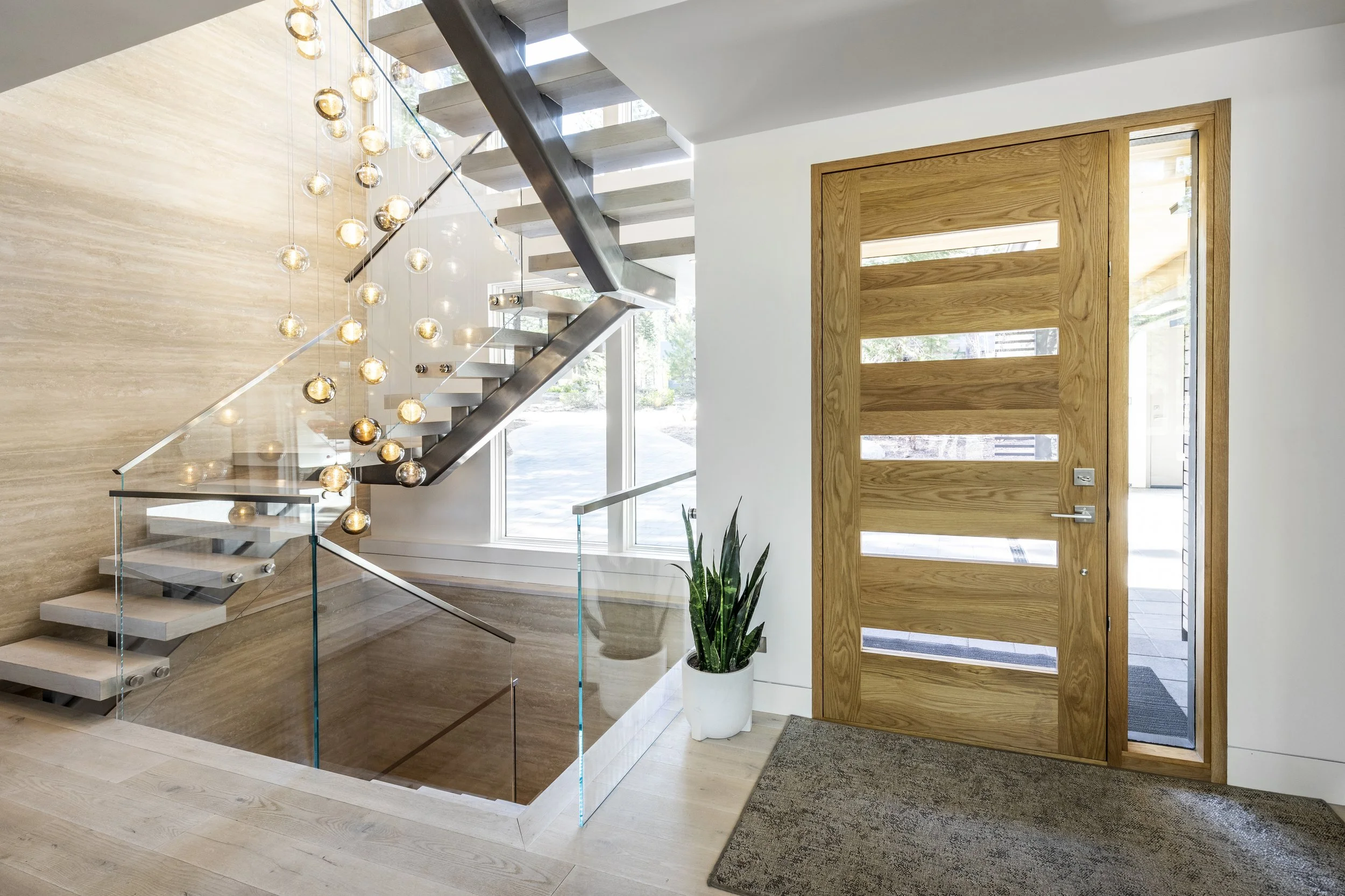 Mountain modern stair with floating treads, glass railings, cedar T&G ceiling, and a custom stunning glass chandelier that cascades down the main level in Martis Camp Truckee CA. Stone walls and custom oak wood floors. Custom oak 5 panel glass front 