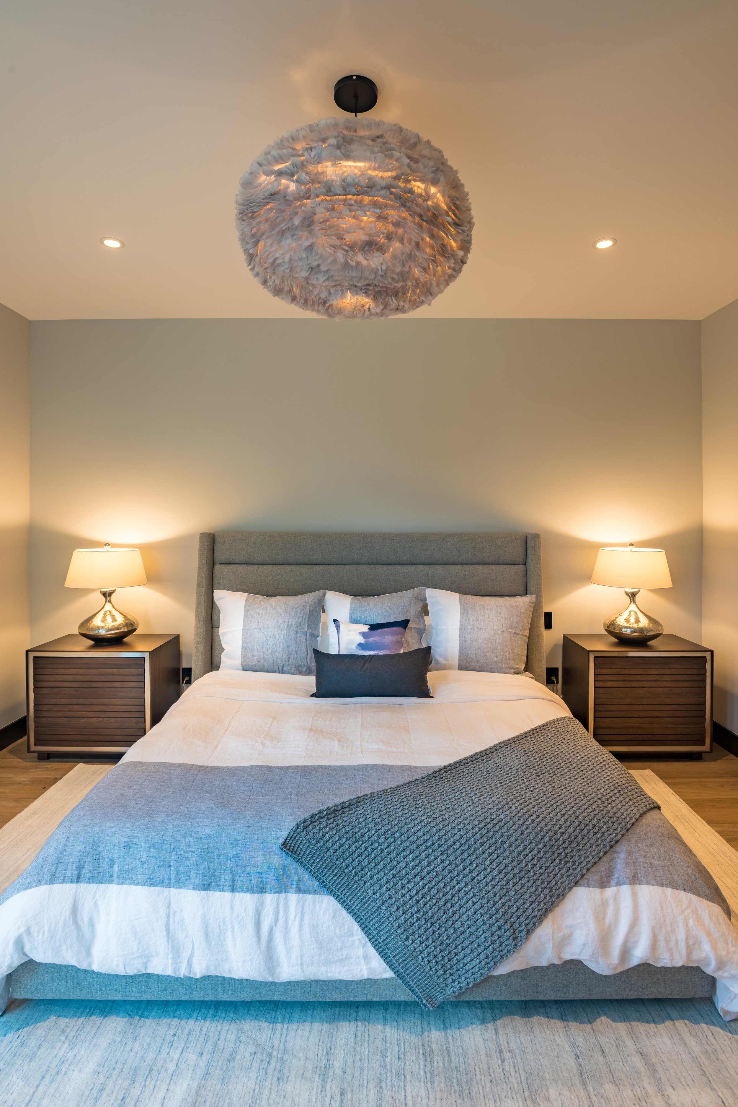 A modern bedroom with a bed, two nightstands with lamps, and a fluffy cloud-like ceiling light fixture.