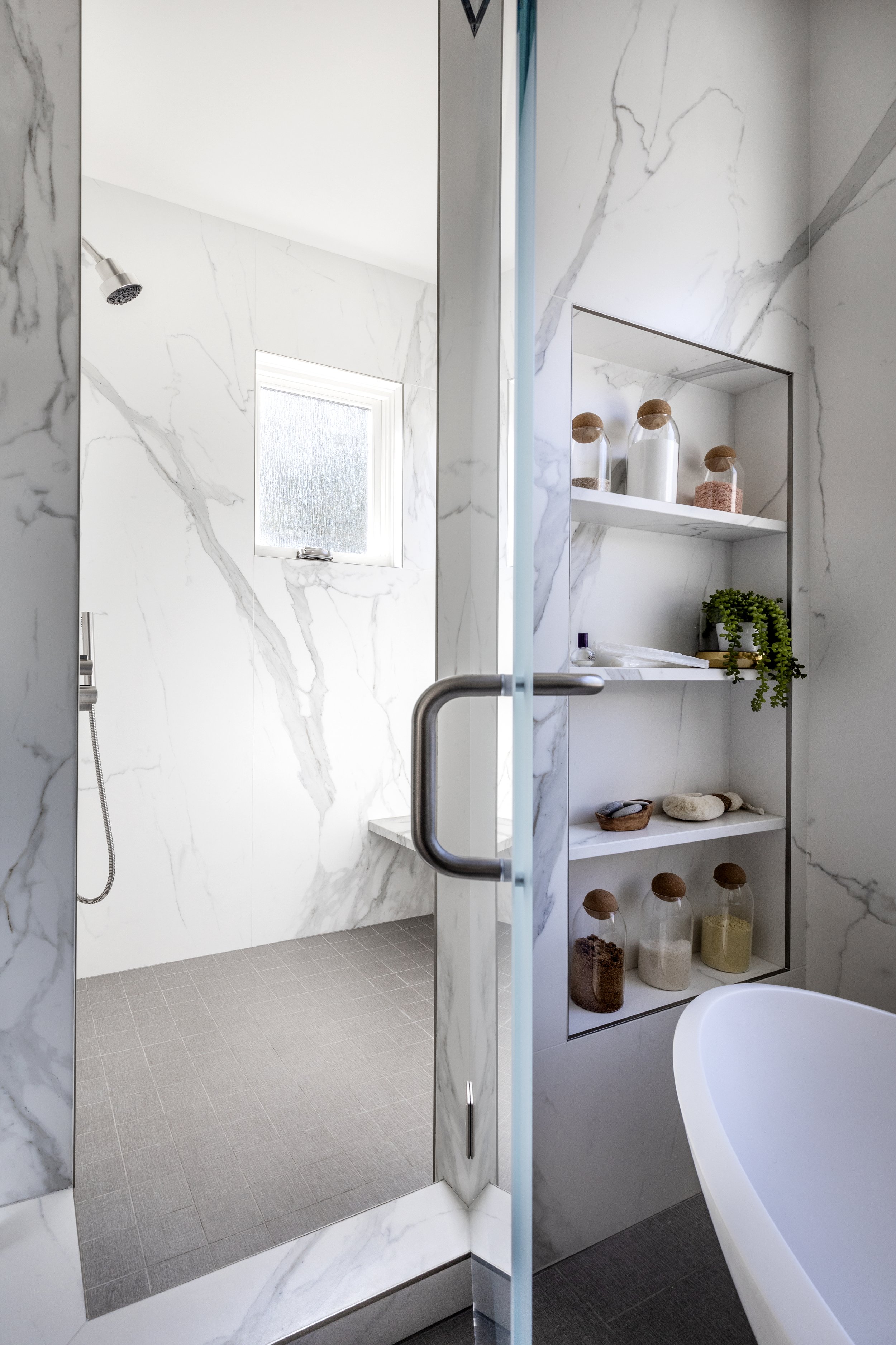 Mountain modern bathroom with luxe freestanding tub seated on top of hydronic heated porcelain grey linen tiles and crystal rock pendants suspended above. Walls are clad in porcelain slabs that look like a Calcutta marble. rain glass obscures to crea