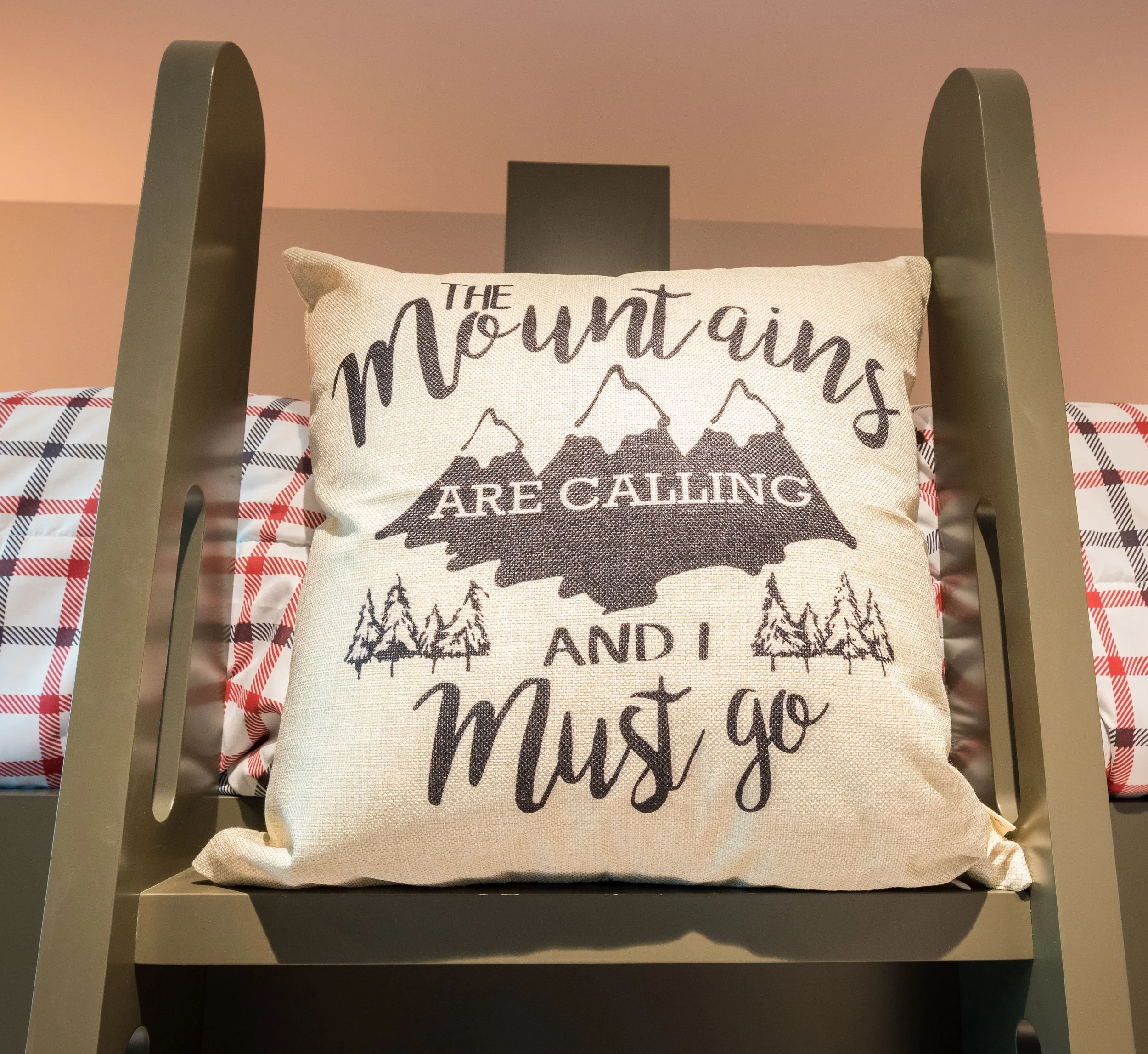 Decorative pillow with outdoor-themed quote on a metal chair, surrounded by plaid blankets.