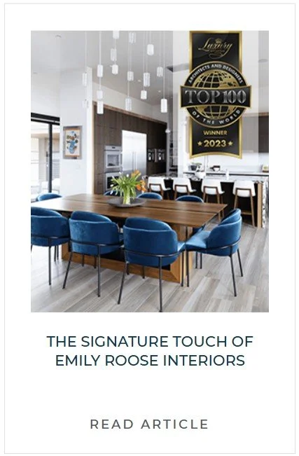 Modern dining room with a wooden table, blue upholstered chairs, and contemporary light fixtures. A large wall decoration with a gold and black badge reads 'Top 100' for 2023.