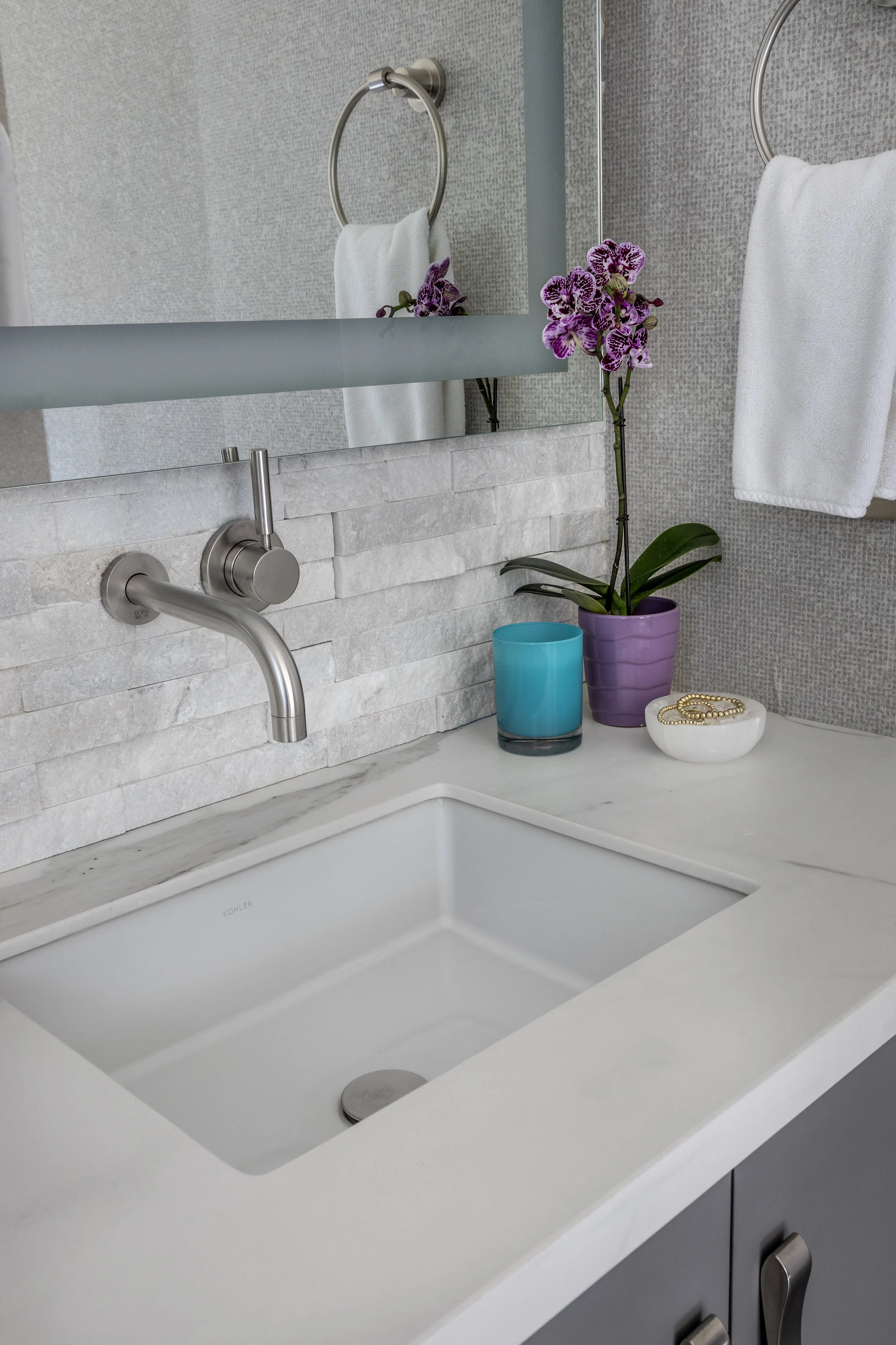 Mountain modern bathroom with vanity wall clad in a white shimmery marble ledger stone and a large LED mirror. The side wall is covered in a natural mica wallpaper. A luxe primary bathroom in Martis Camp in Truckee, CA. 
