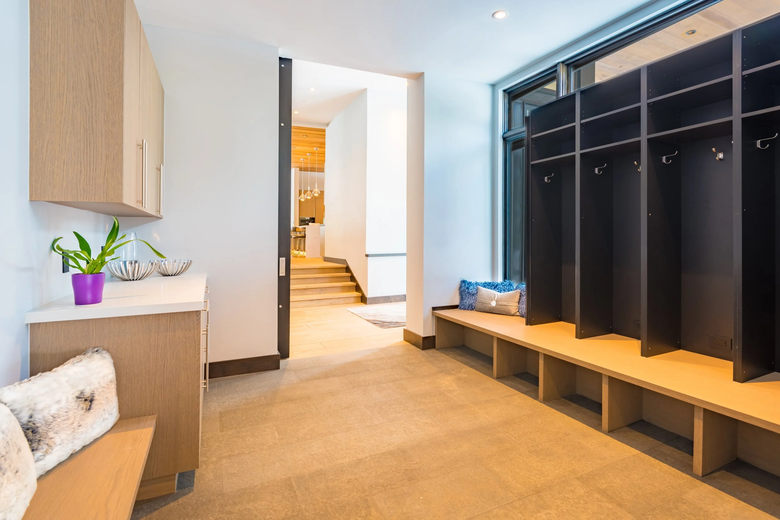 Modern indoor space with wooden benches, black cubbies, a small table with a purple pot and green plant, and stairs leading to another room.