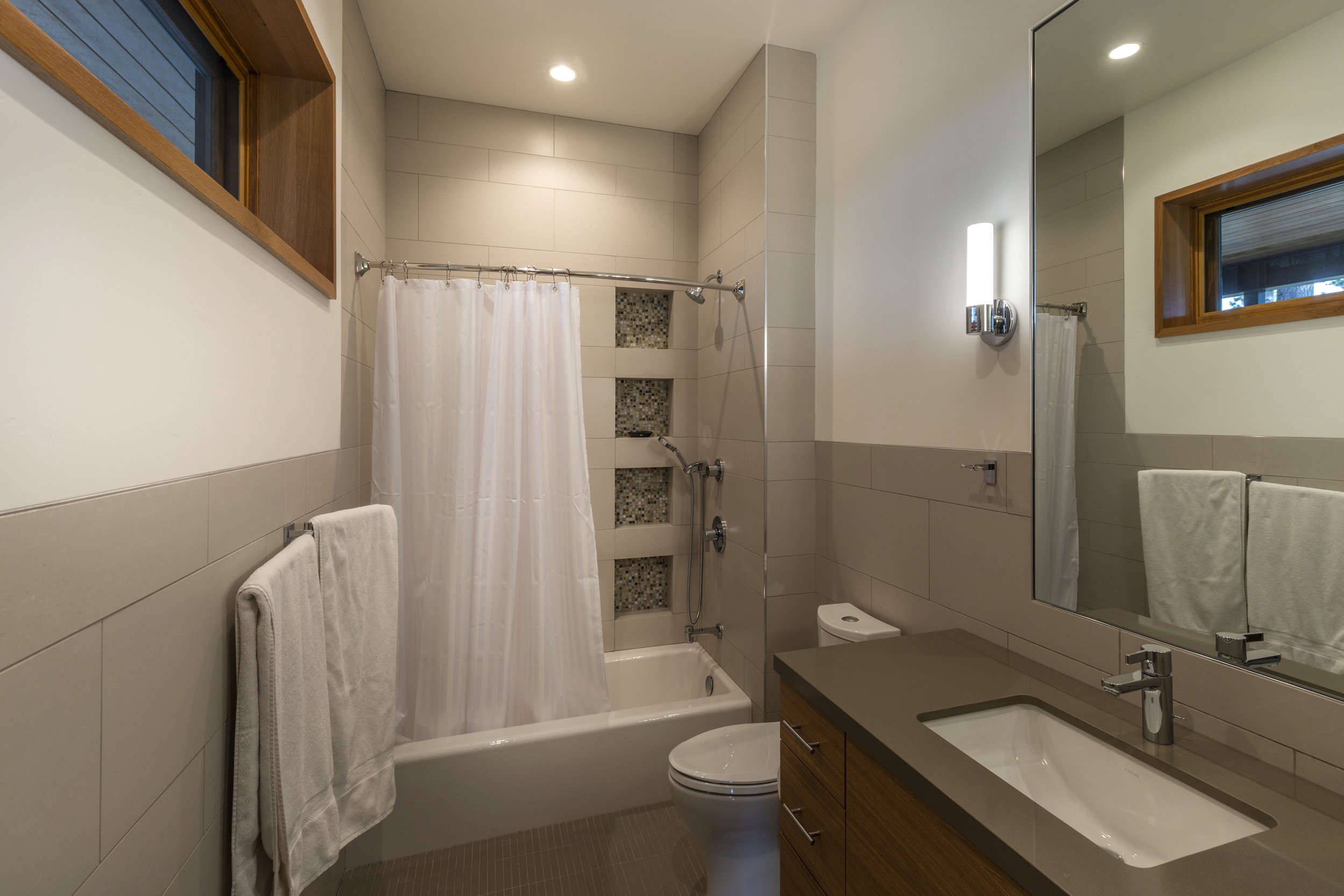 Bathroom with bathtub, shower curtain, toilet, sink, large mirror, small window, and towel racks.