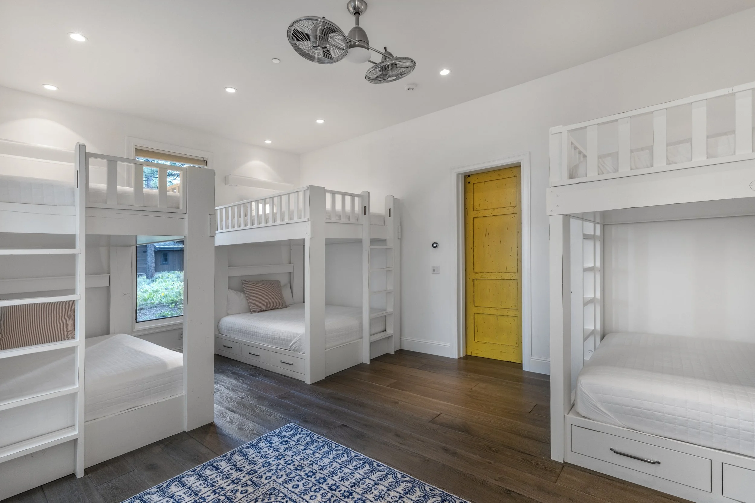 Bedroom with white bunk beds, a yellow door, wood flooring, and a blue patterned rug.