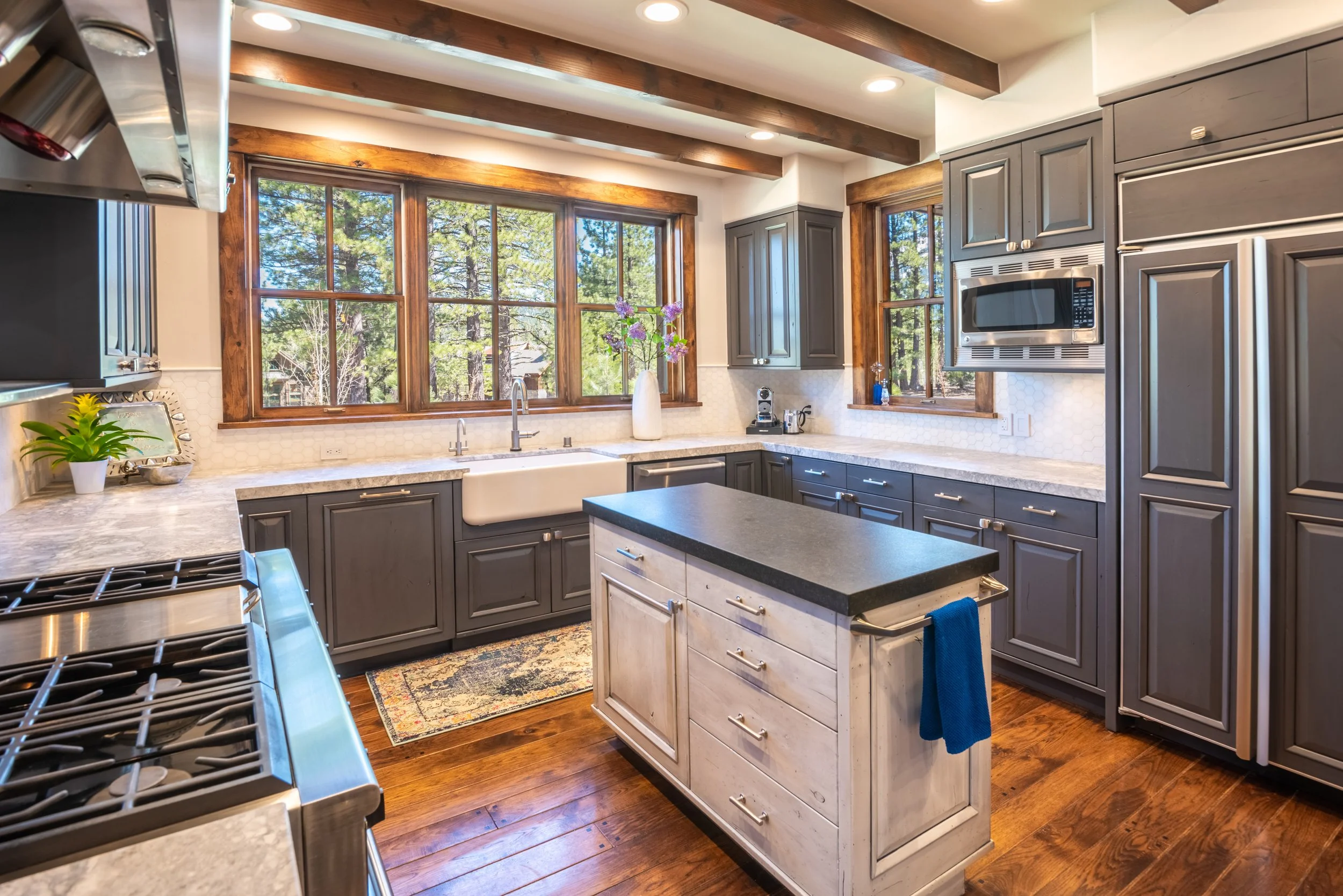 Kitchen with wooden beams, gray cabinets, large windows, and a central island.