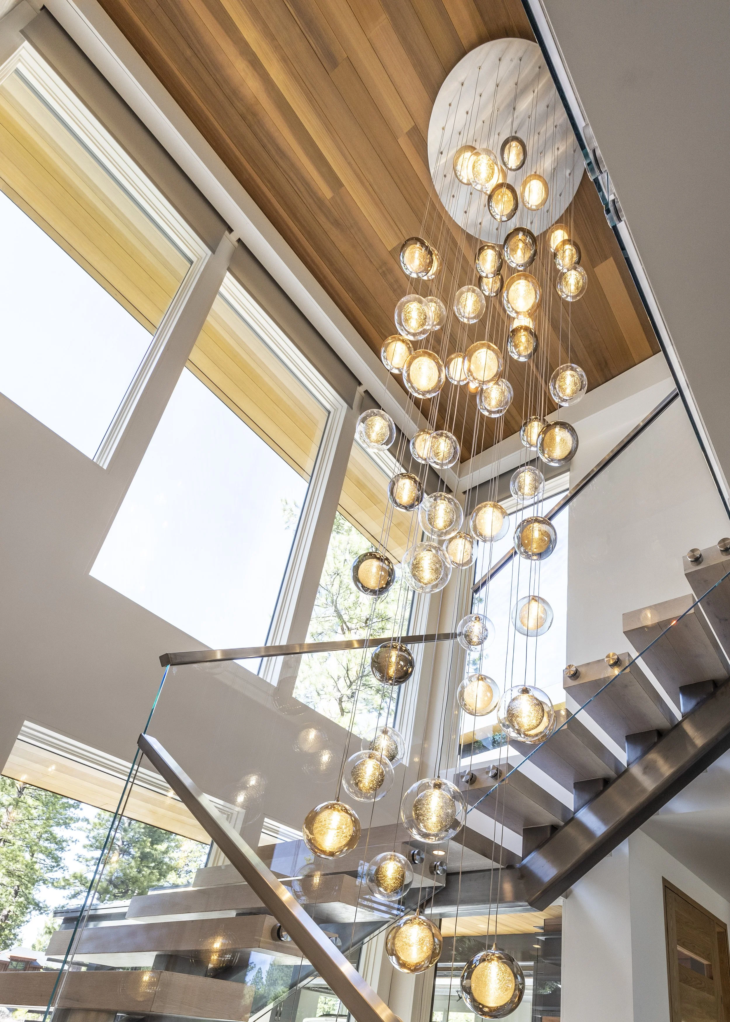 Mountain modern stair with floating treads, glass railings, cedar T&G ceiling, and a custom stunning glass chandelier that cascades down the main level in Martis Camp Truckee CA. 