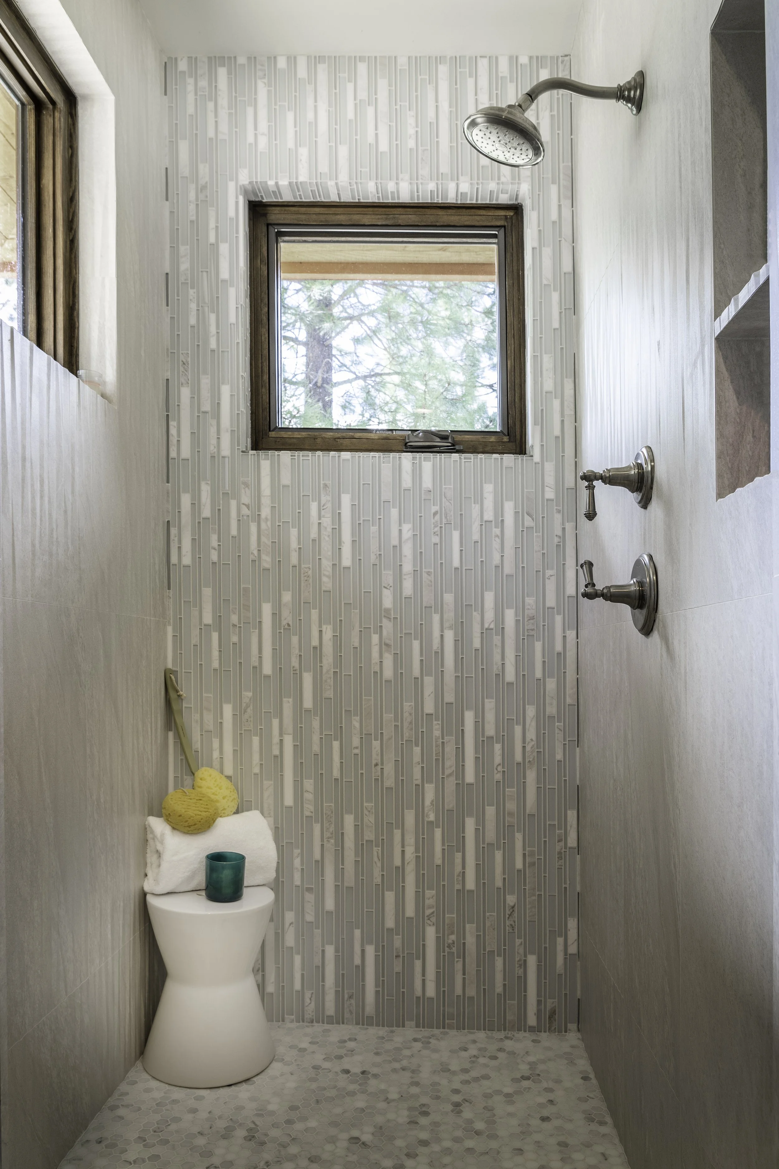 Primary shower with a window, tiled walls with an accent glass tile mosaic, and two showerheads