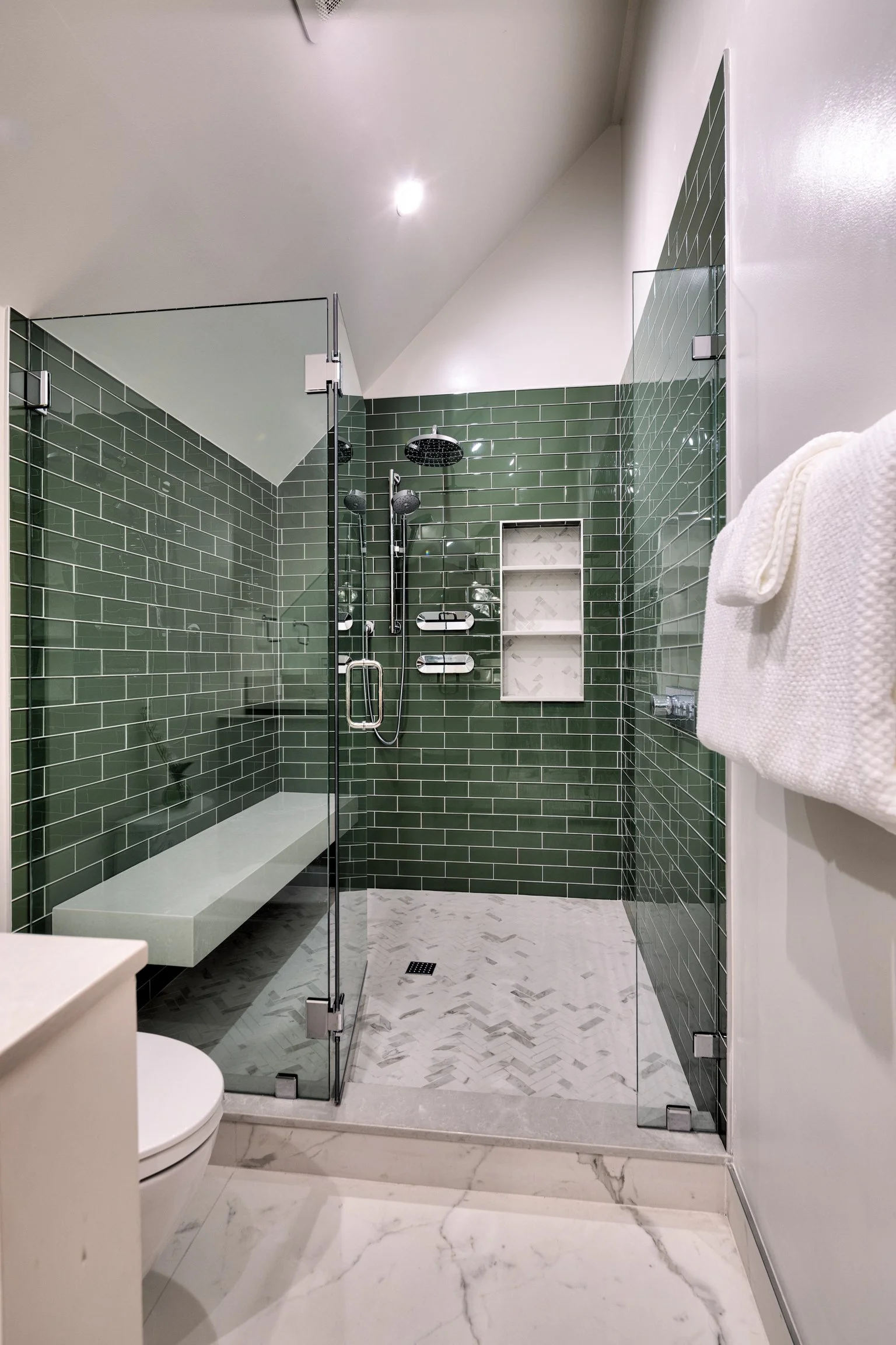 Modern bathroom with green tiled walk-in shower, clear glass walls, marble floor, and white walls.