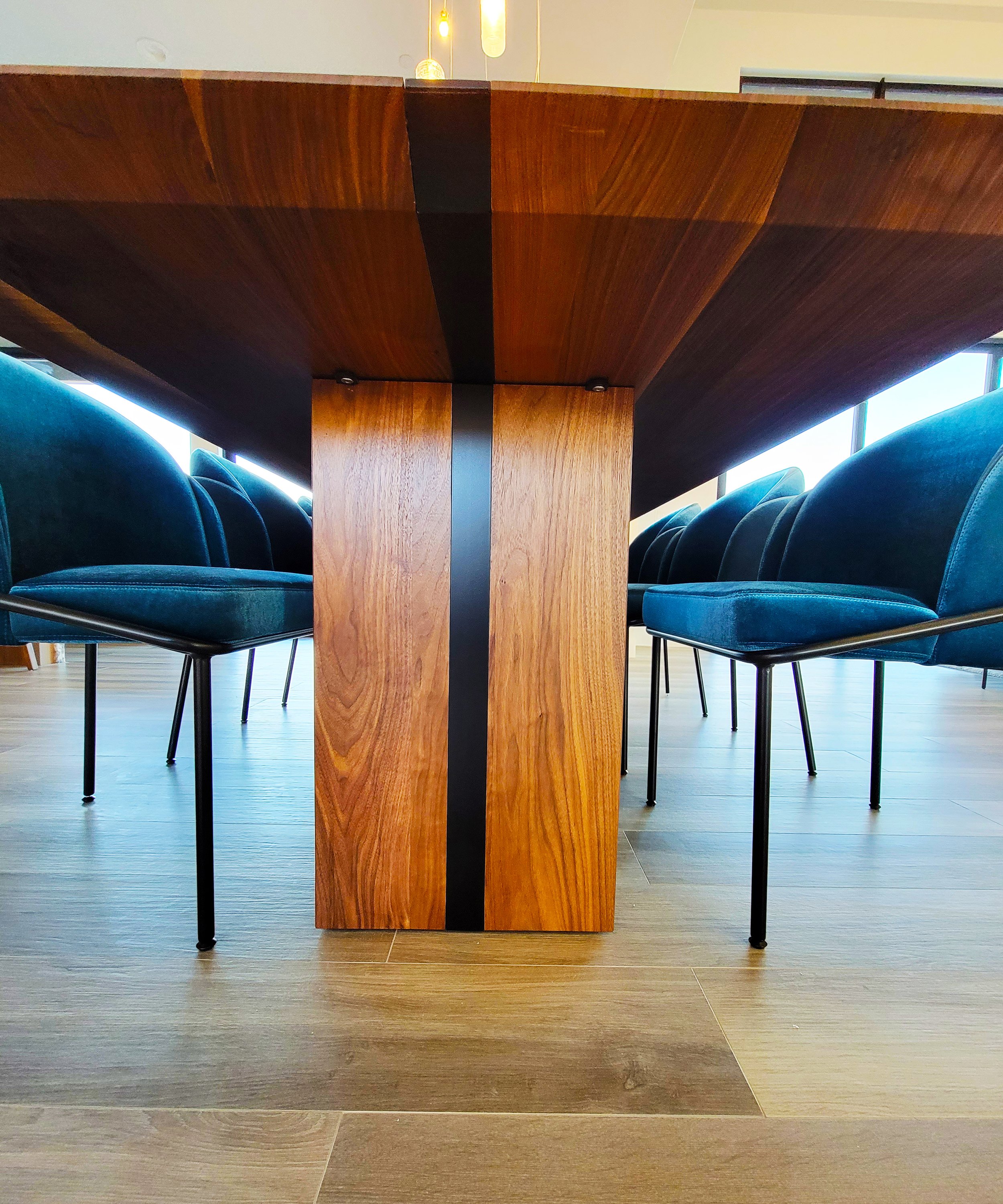 View from below of a wooden dining table with a black stripe running down the center, surrounded by blue chairs with black legs in a modern dining area.
