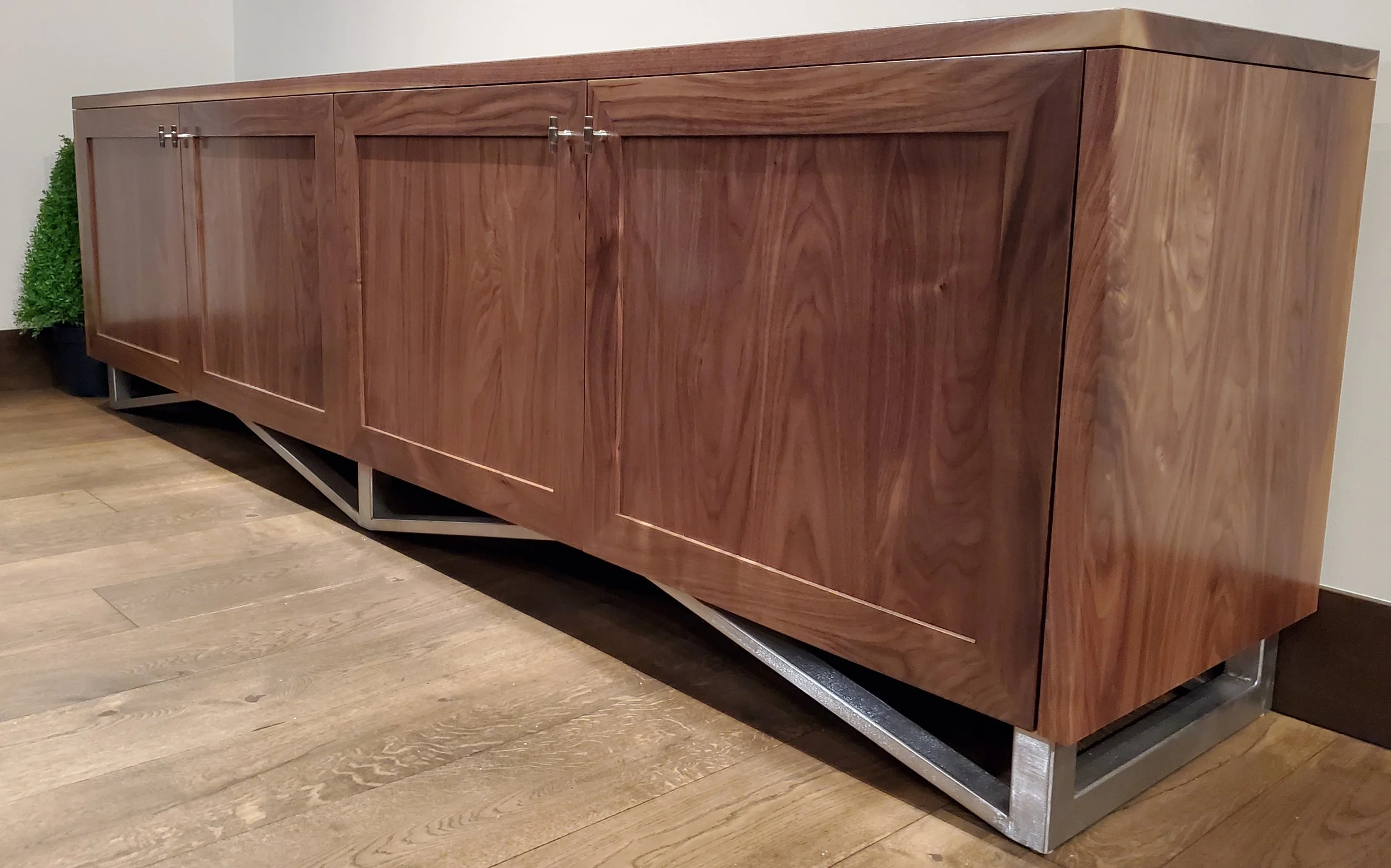 A wooden sideboard with metal legs placed against a wall in a room with wooden flooring.