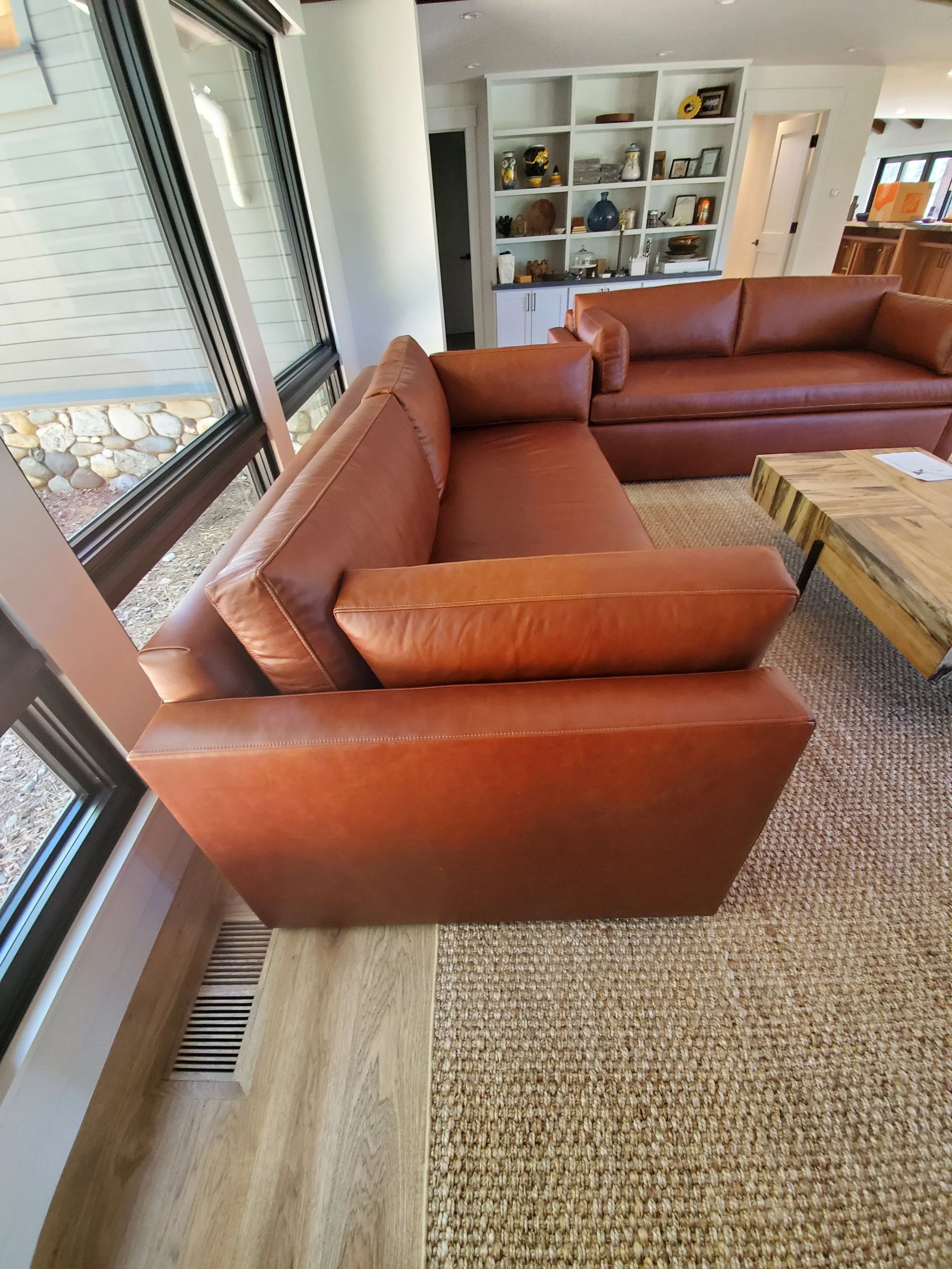 Living room with two brown leather sofas, a wooden coffee table, a large window, and built-in white shelves with decorative items.
