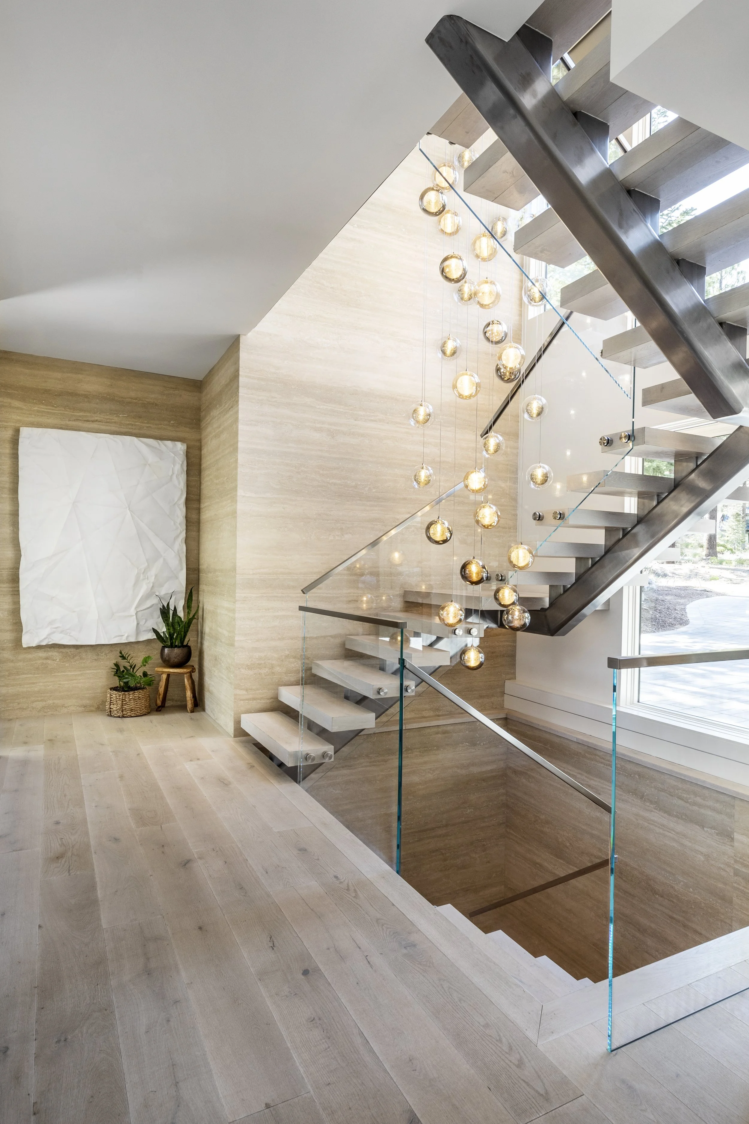 Mountain modern stair with floating treads, glass railings, cedar T&G ceiling, and a custom stunning glass chandelier that cascades down the main level in Martis Camp Truckee CA. Stone walls and custom oak wood floors.