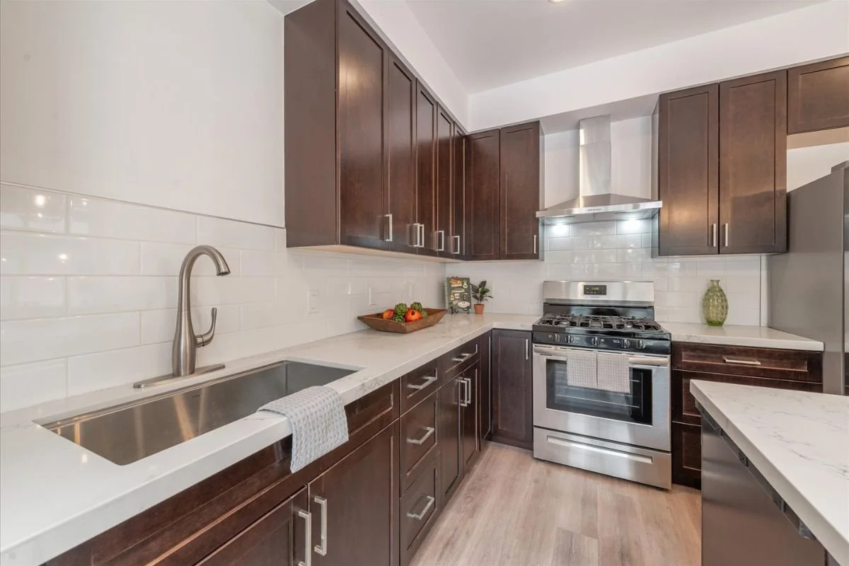 Modern kitchen with dark wood cabinets, stainless steel oven and stove, white countertops, white tiled backsplash, and minimal decorative items.