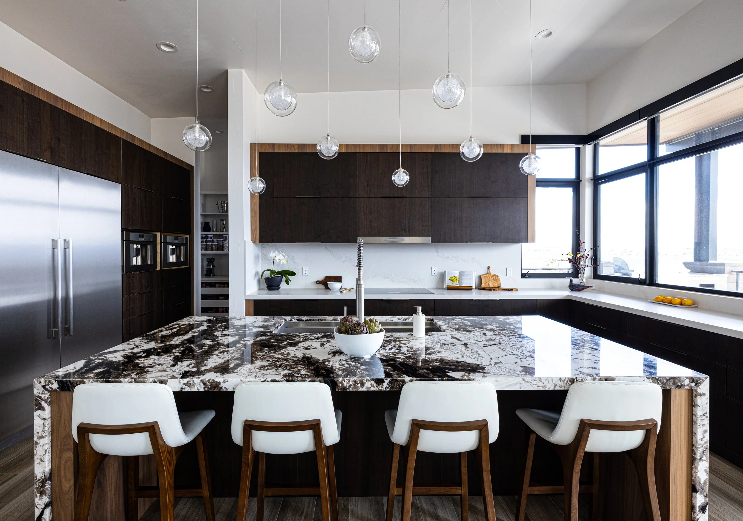 Modern kitchen with marble island, dark wood cabinets, stainless steel refrigerator, and large windows