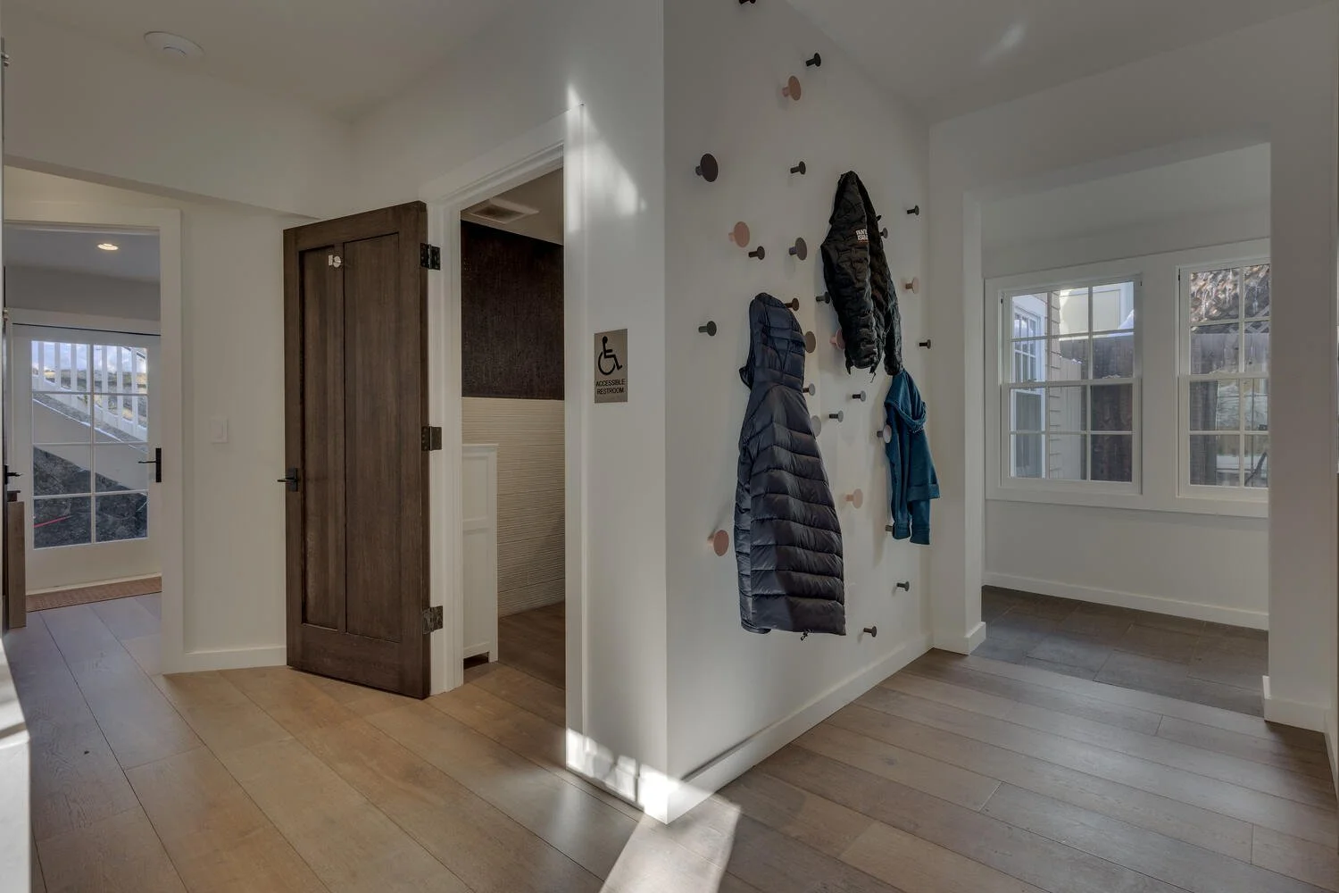Entryway with coat hooks, jackets hanging, wooden door, window, and hardwood flooring