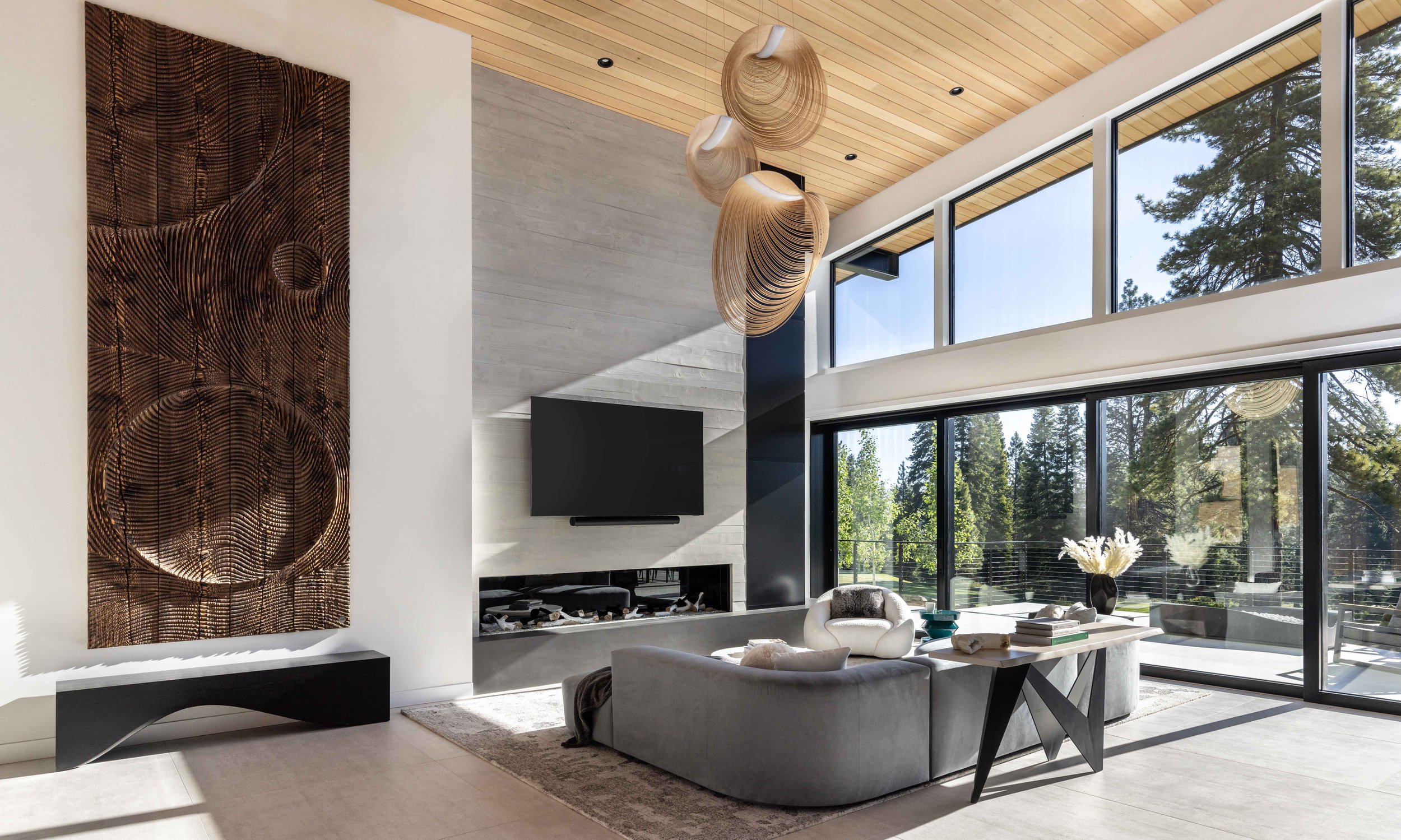 Modern living room with large windows, beige and gray furniture, abstract wall art, and hanging wooden light fixtures.
