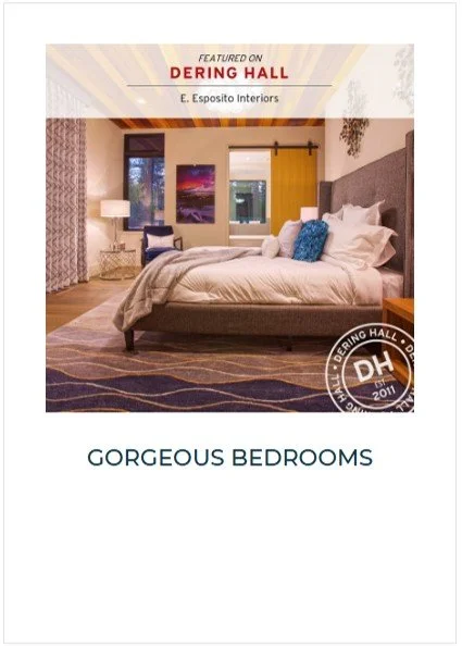 A cozy bedroom with a neatly made bed, featuring white bedding and blue pillows. The room has large windows, a nightstand, a chair, and decorative elements, creating a warm and inviting atmosphere.