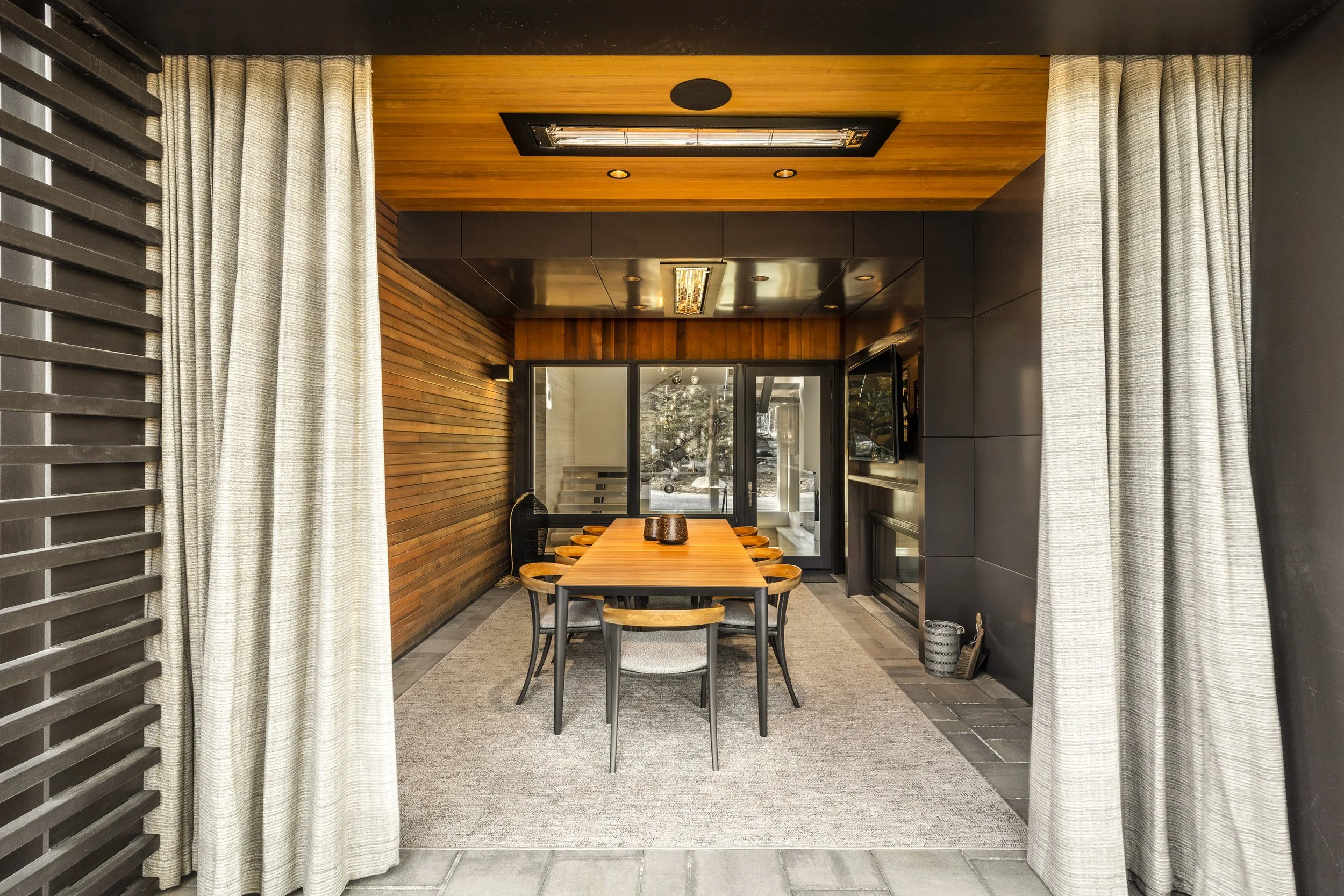 Mountain modern outdoor dining room with 2 way fireplace, heaters in the ceiling for year-round use, and decorative outdoor draperies to keep the space cozy and warm during the colder months in Martis Camp in Truckee, CA.