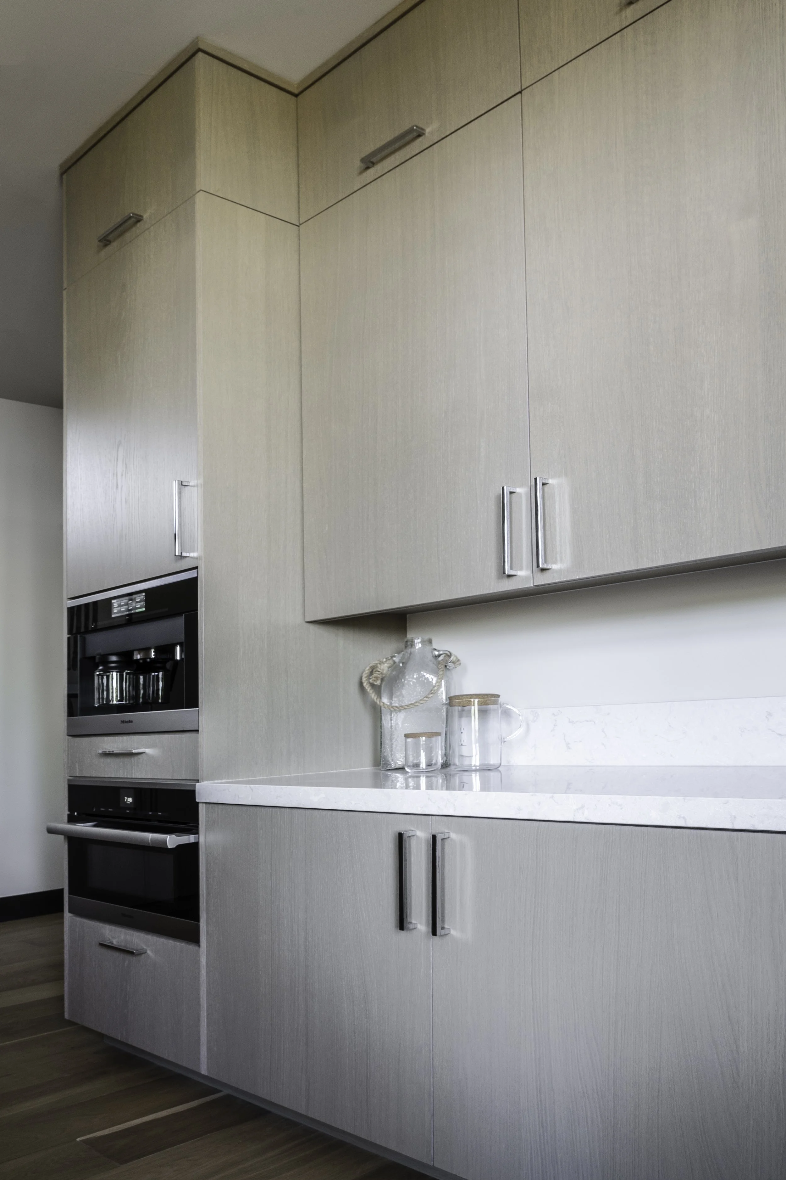 Kitchen cabinets with a built-in oven, glass jars, and a pitcher on the countertop.