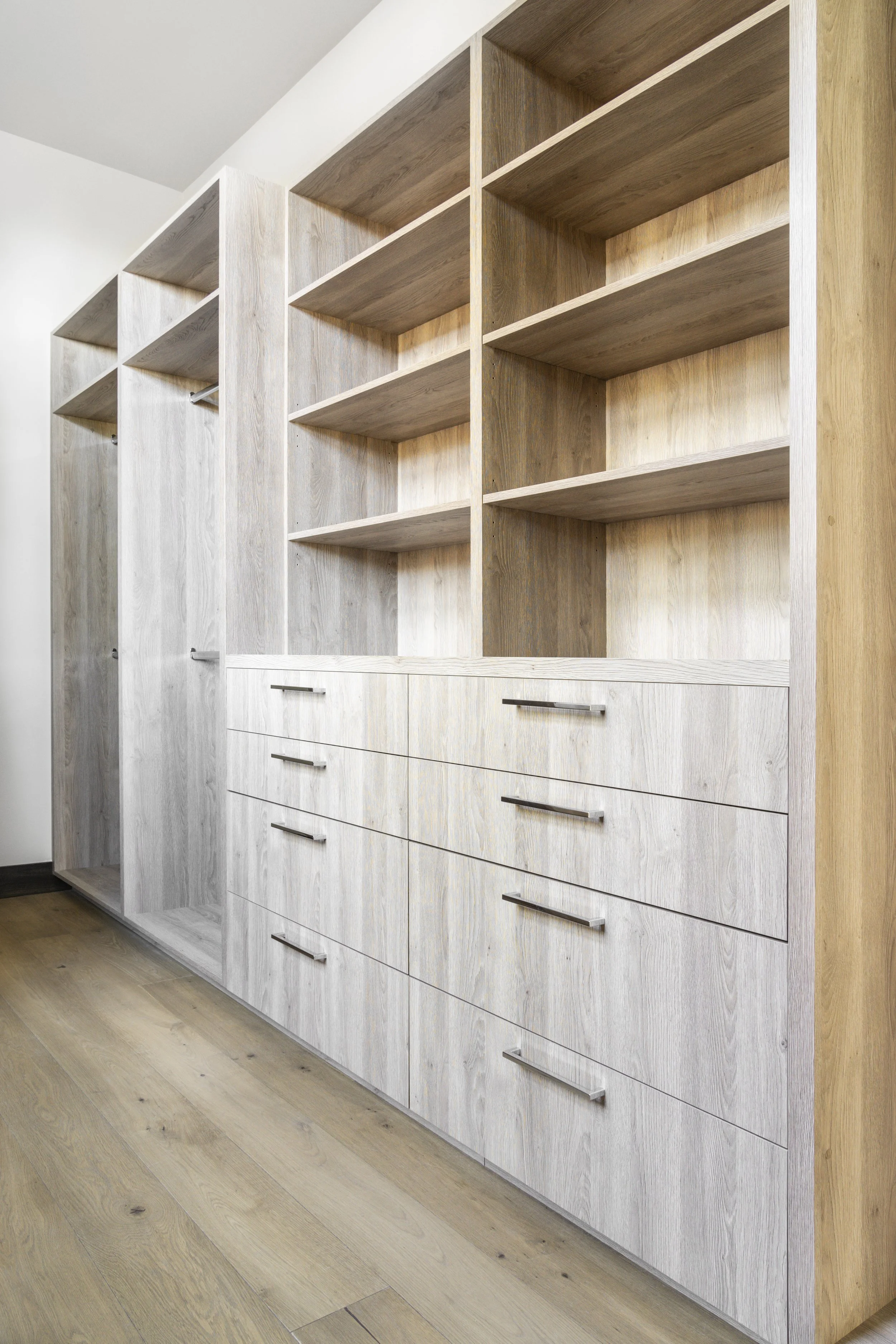 Empty built-in wooden bookshelf and cabinet with open shelves, drawers, and hanging space near the ceiling in a room.