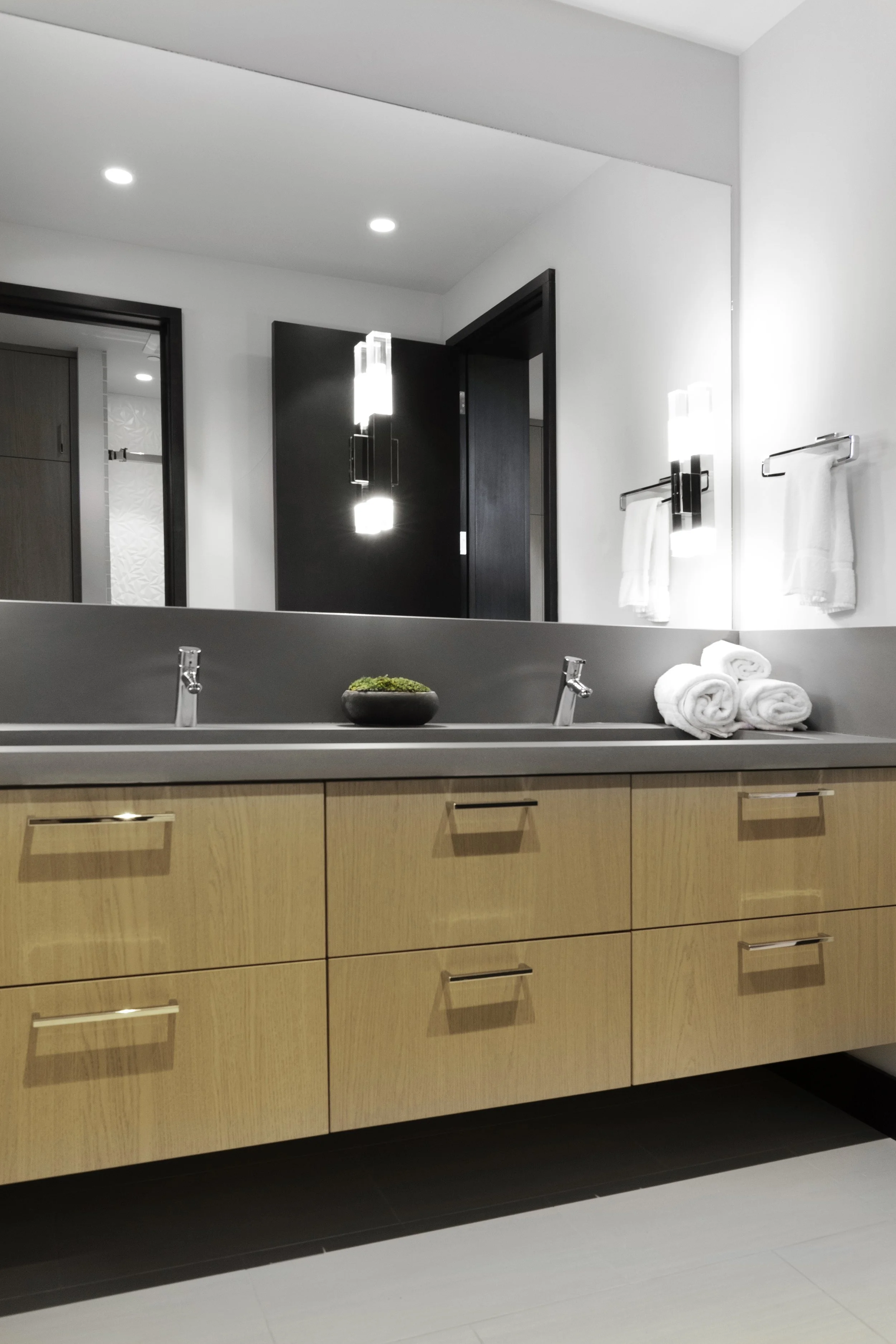 Modern bathroom with a large mirror, wooden vanity with multiple drawers, double sinks, and towel racks with towels.