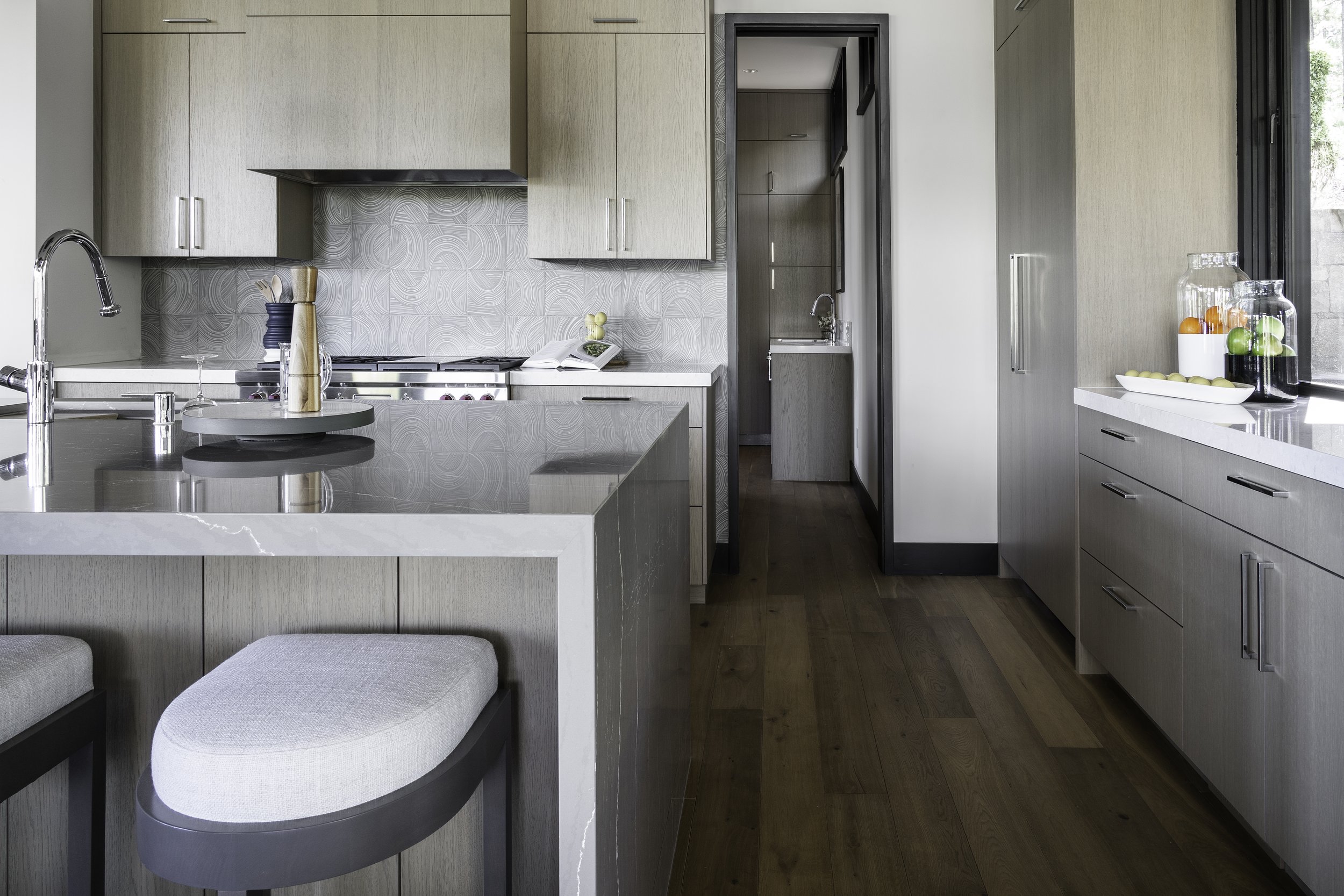 Modern kitchen with light wood flat panel cabinets, quartz  marble looking countertops, stainless steel Wolf and Sub-Zero appliances, and a window with a view of the Lake Tahoe mountain landscape.