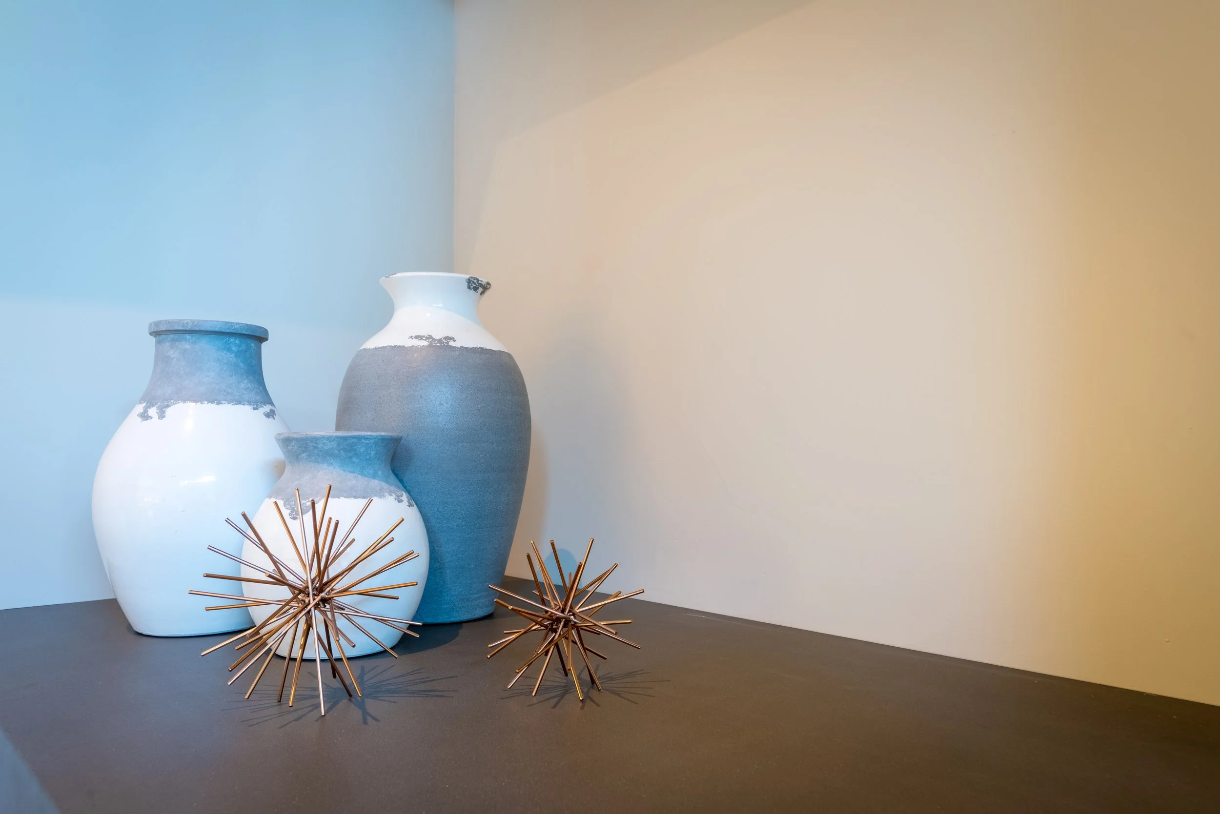 Three ceramic vases with a blue and white glaze and decorative spiky metallic ornaments on a dark surface against a gradient wall background.