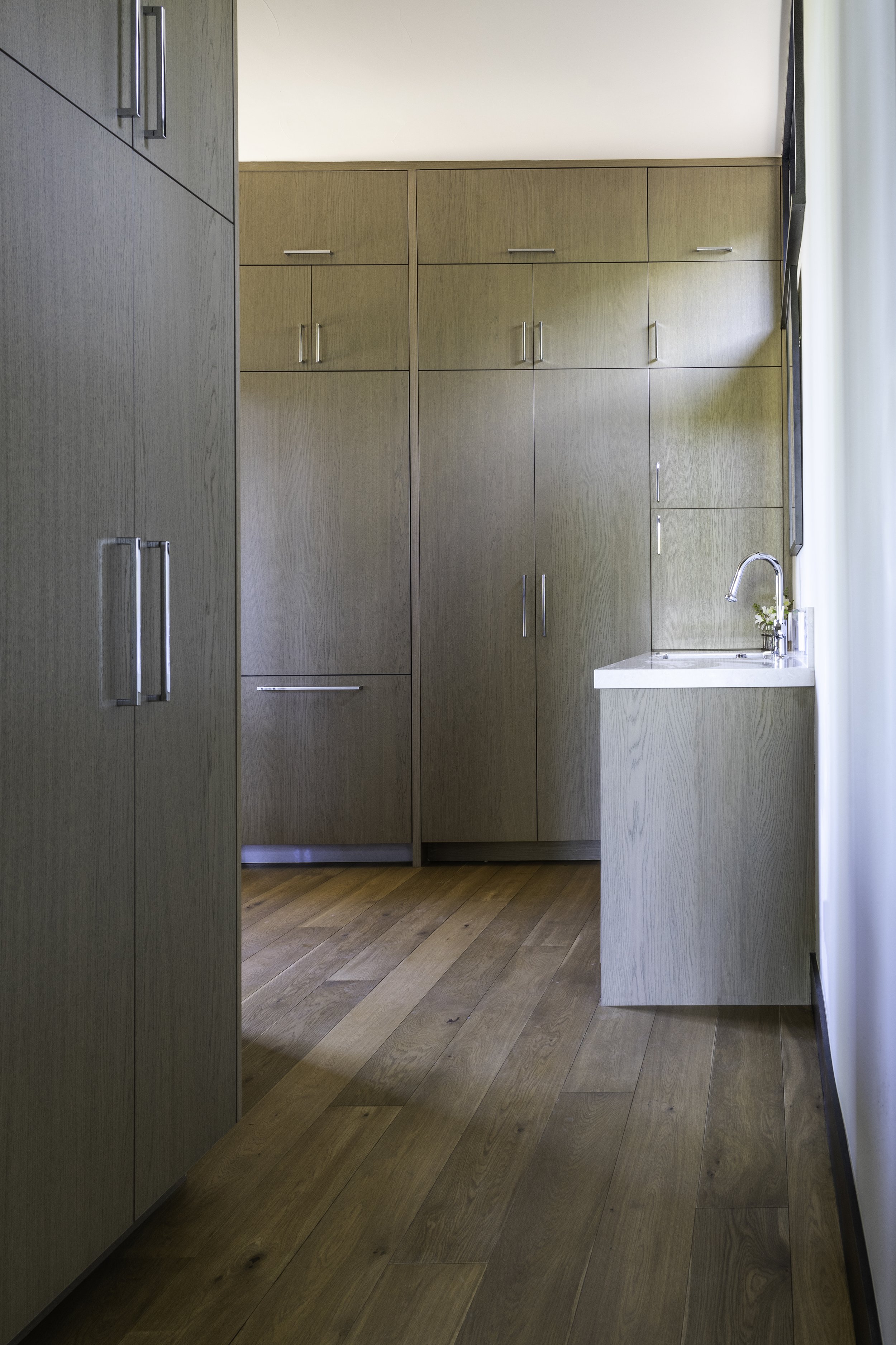 A modern kitchen with wooden cabinets, a small countertop with a faucet, and hardwood flooring.