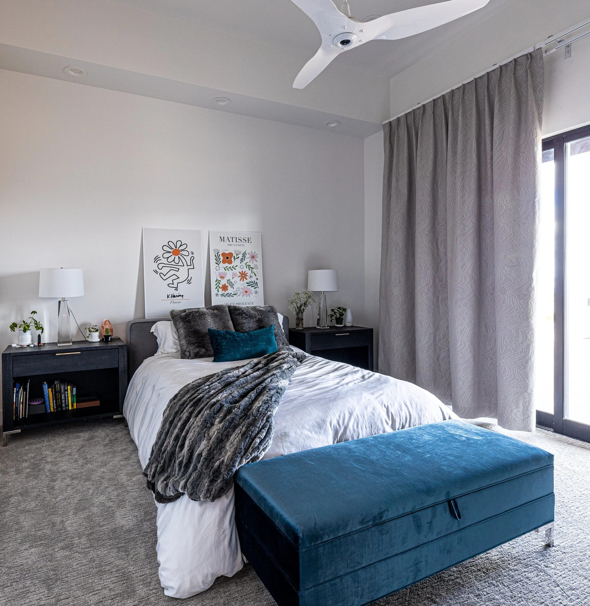 Bedroom with a bed, two nightstands with lamps, artwork, and a teal bench at the foot of the bed.