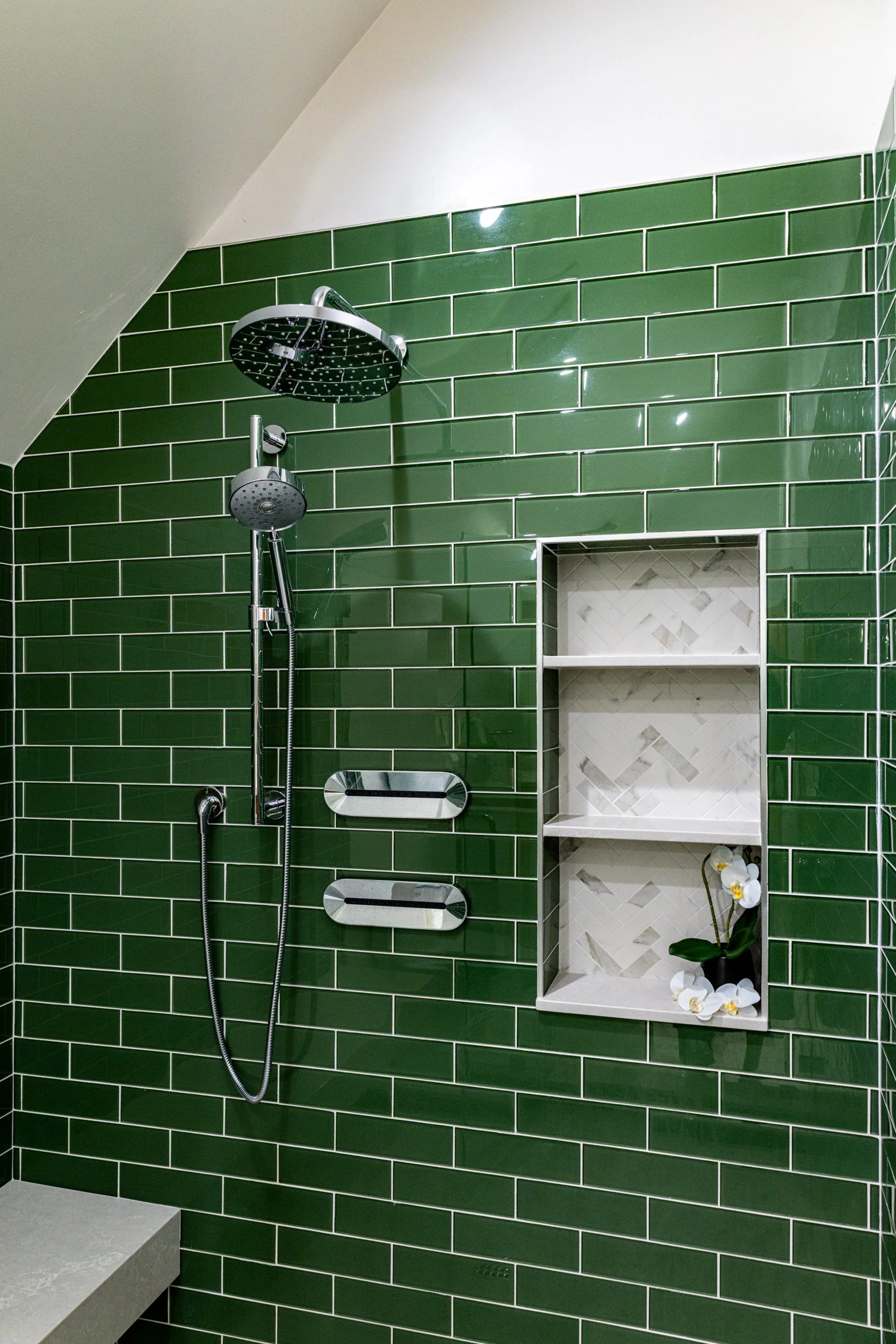 Green tiled shower with a built-in shelf holding a potted white orchid, and a ceiling-mounted rain showerhead with an adjustable handheld shower.