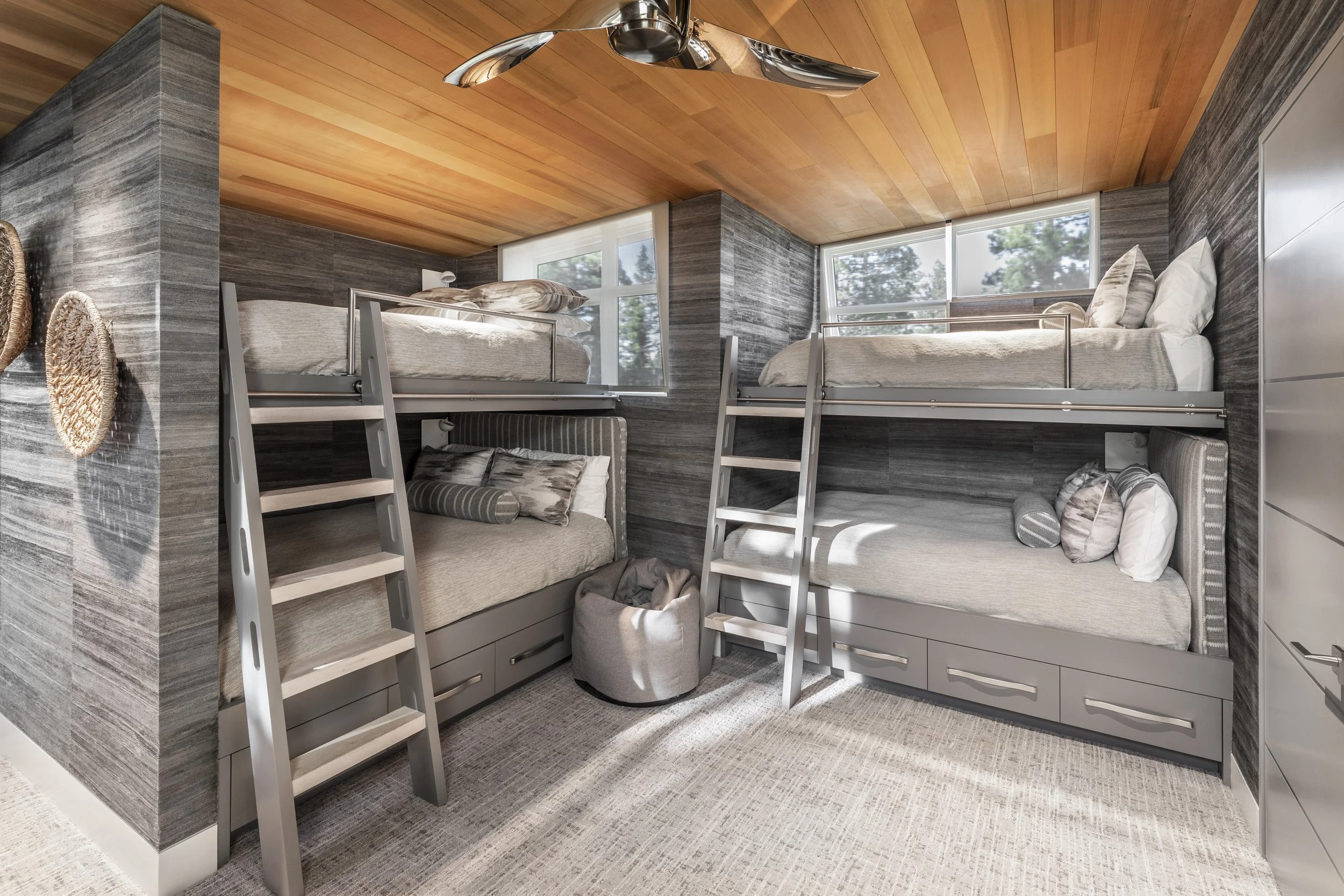 Mountain modern bunk room with natural wood wallpaper, cedar ceiling and custom designed and built-in bunk beds with storage drawers and library ladders in Martis Camp Truckee CA.