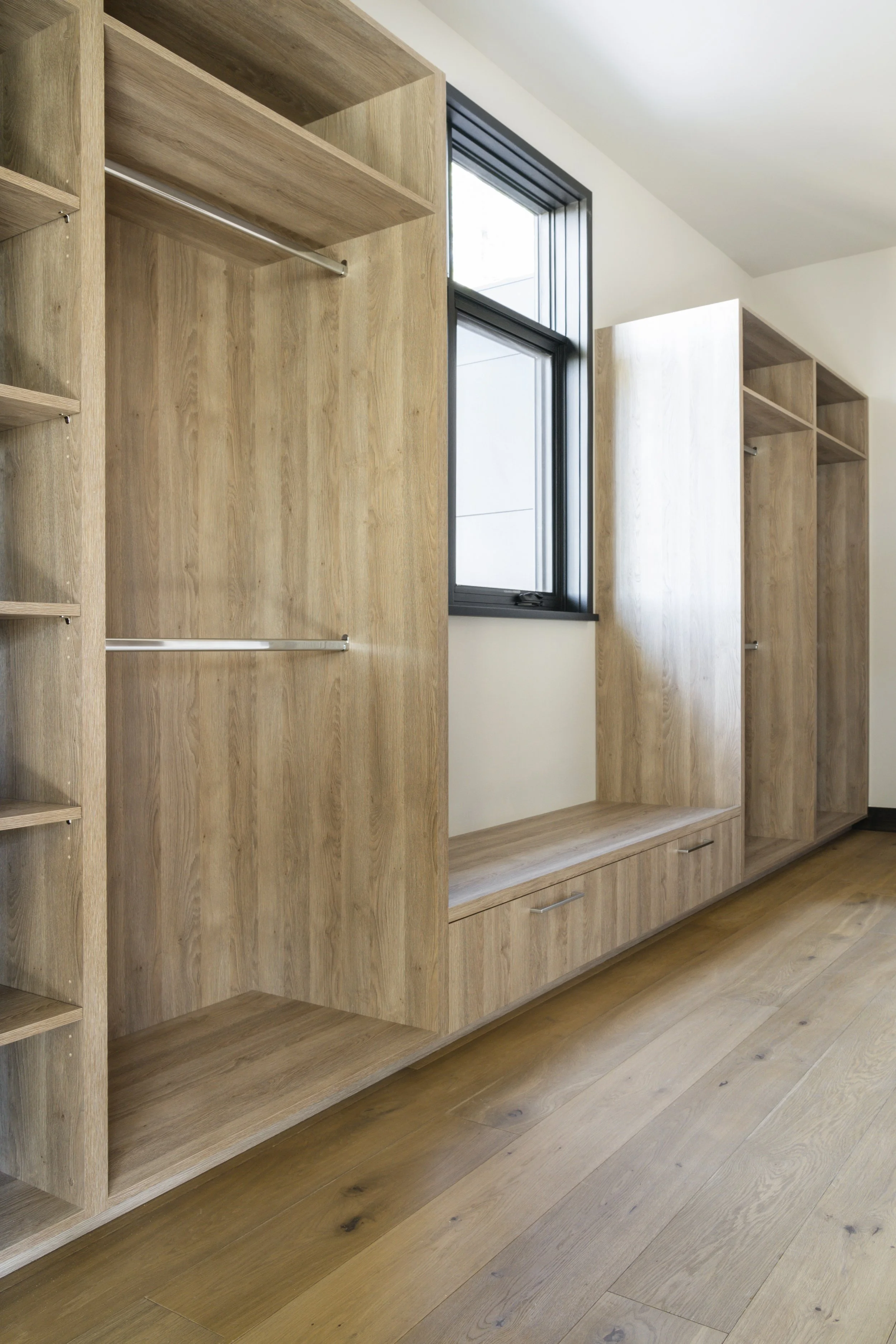 Wooden built-in wardrobe and bench near a window, with open shelves and hanging space.