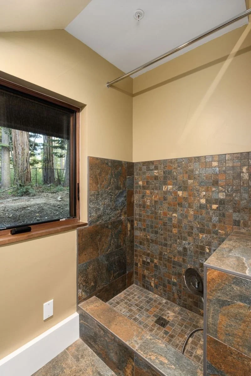 A bathroom shower with brown and gray stone tiles, a small window, and a beige wall.