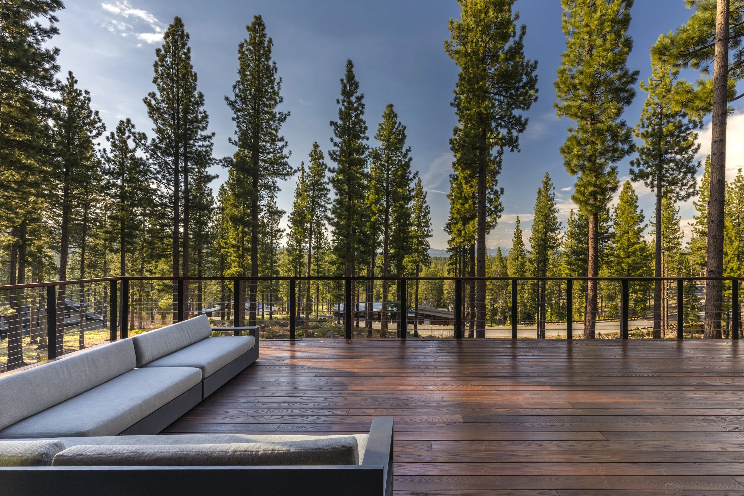 A spacious wooden deck with gray outdoor sectional sofa overlooking a forest of tall pine trees.