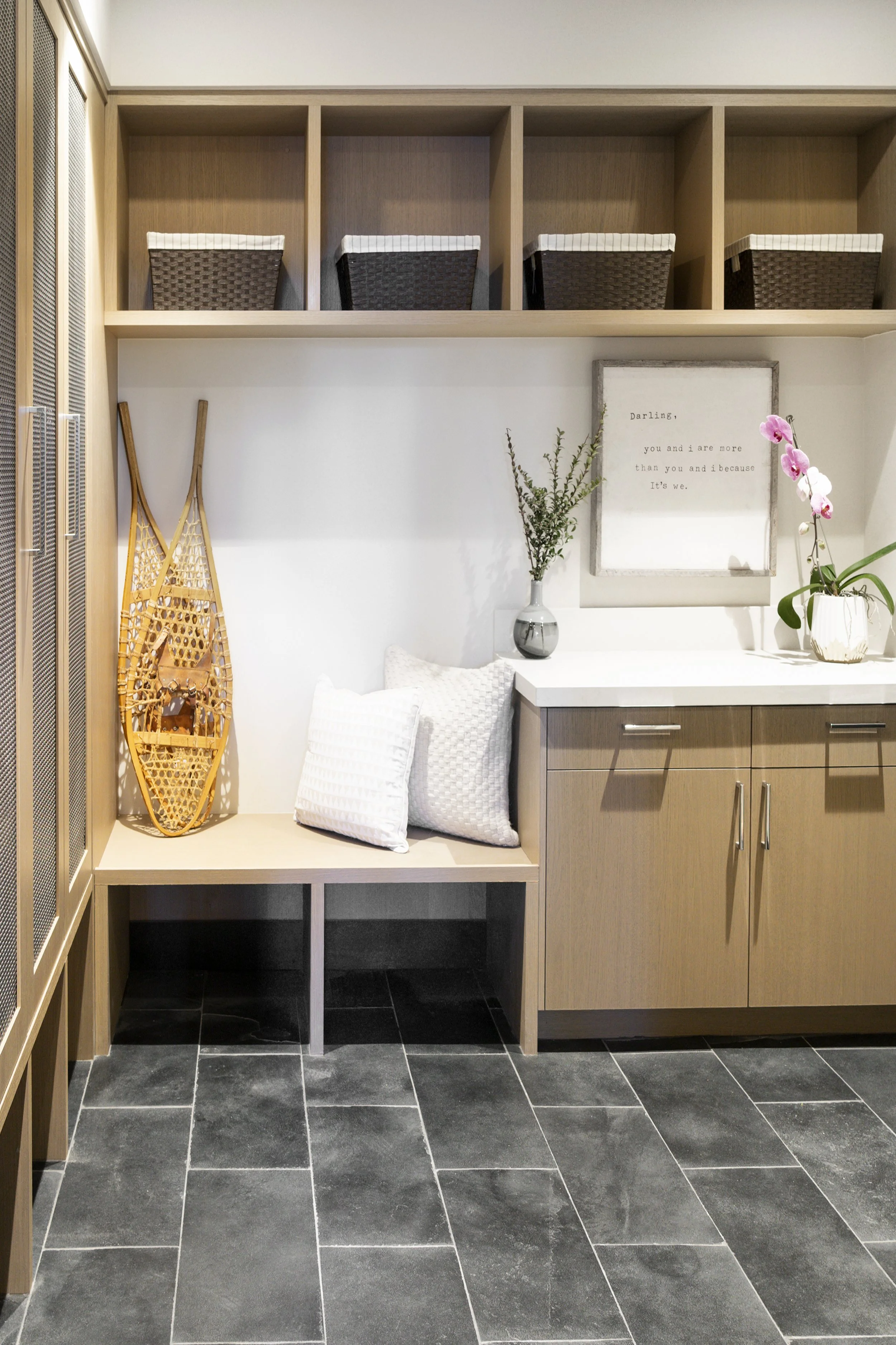 A modern interior corner with a wooden bench, pillows, decorative items, framed quote, and plants on a white countertop.
